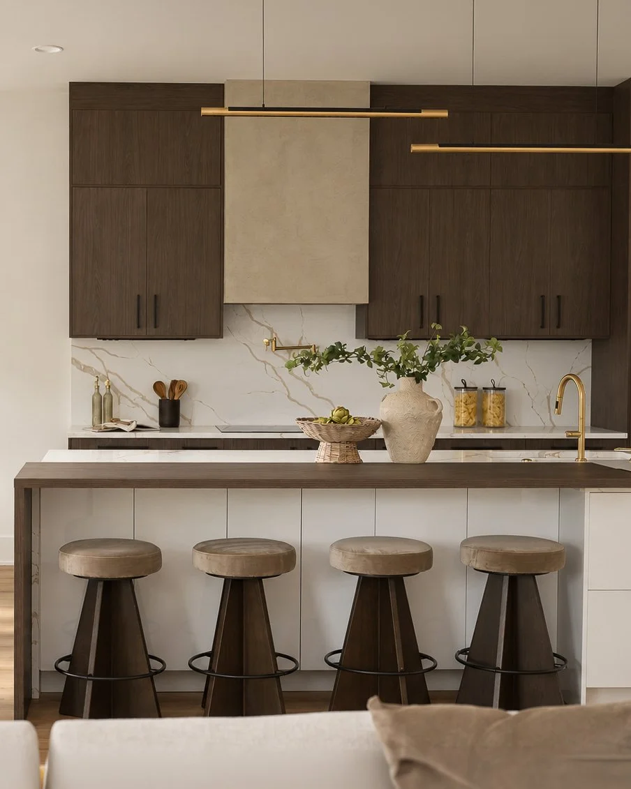 Modern kitchen with dark wood cabinets, a white marble backsplash with gold veins, a large vase with green foliage, a basket of apples, minimal decorative items, and a white island with four wooden bar stools.