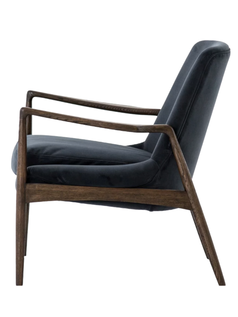 Side view of Mid-century modern accent chair upholstered in dark navy blue velvet with a tall backrest, plush seat cushion, and exposed dark wood frame with slender arms and tapered legs.