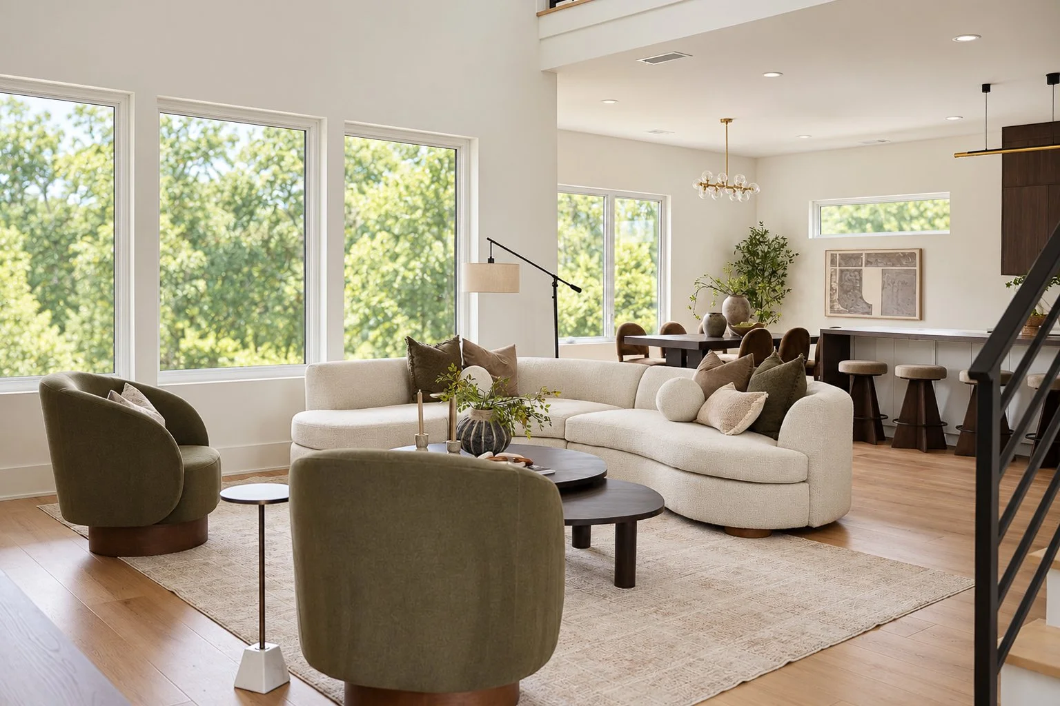Modern living room with large windows, white sectional sofa, green armchairs, black coffee table, and a dining area with a wooden table and chairs.