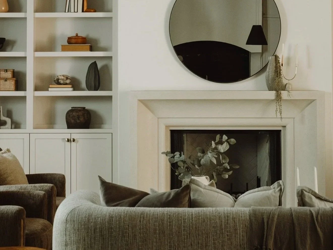 Living room with a fireplace, a large round mirror above it, and built-in shelves with decorative items.
