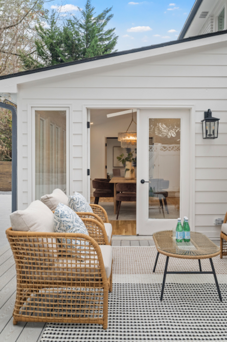 Outdoor patio with rattan seating, cushions, a small table with bottled water, and sliding glass doors leading to an indoor dining area.