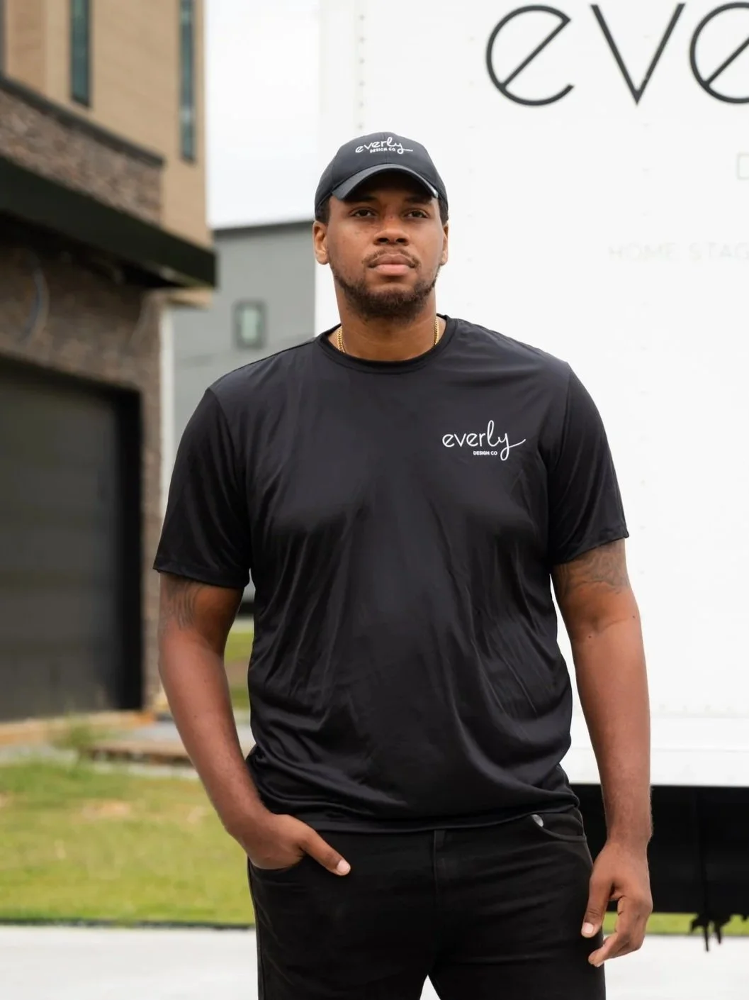 A man standing outdoors wearing a black t-shirt and cap with the brand name 'Everly' printed on them, in front of a white truck with partial text 'eve' visible.
