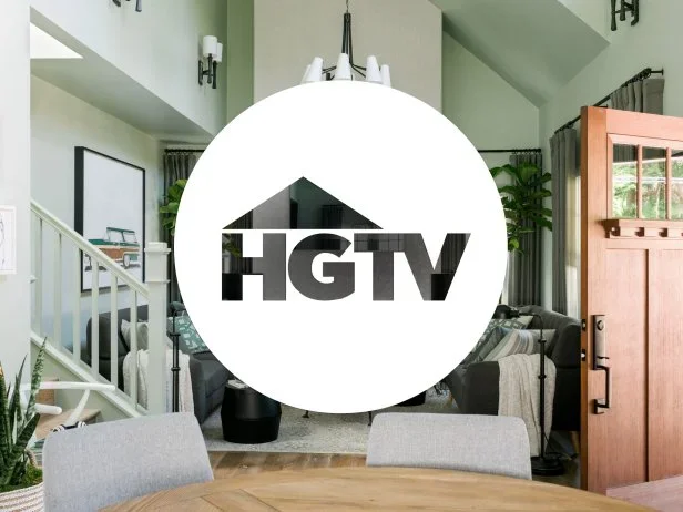 Living room with gray chairs, a dining table, a staircase, potted plants, and a large HGTV logo in the center.