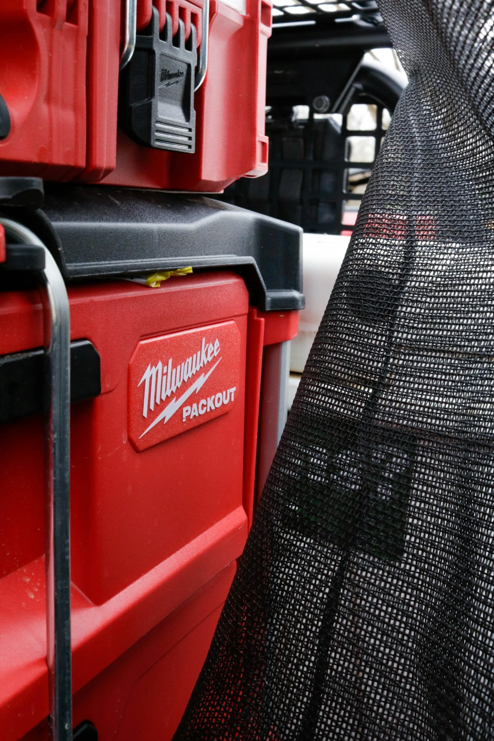 Close-up of red Milwaukee Packout toolbox and other tool storage containers, with part of black mesh material in the foreground.