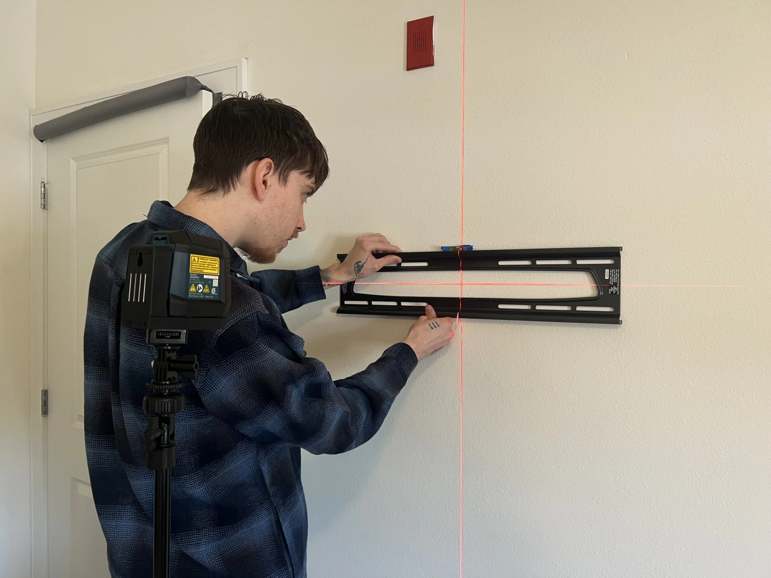 A man measuring a wall with a level, with a red laser line projected on the wall.
