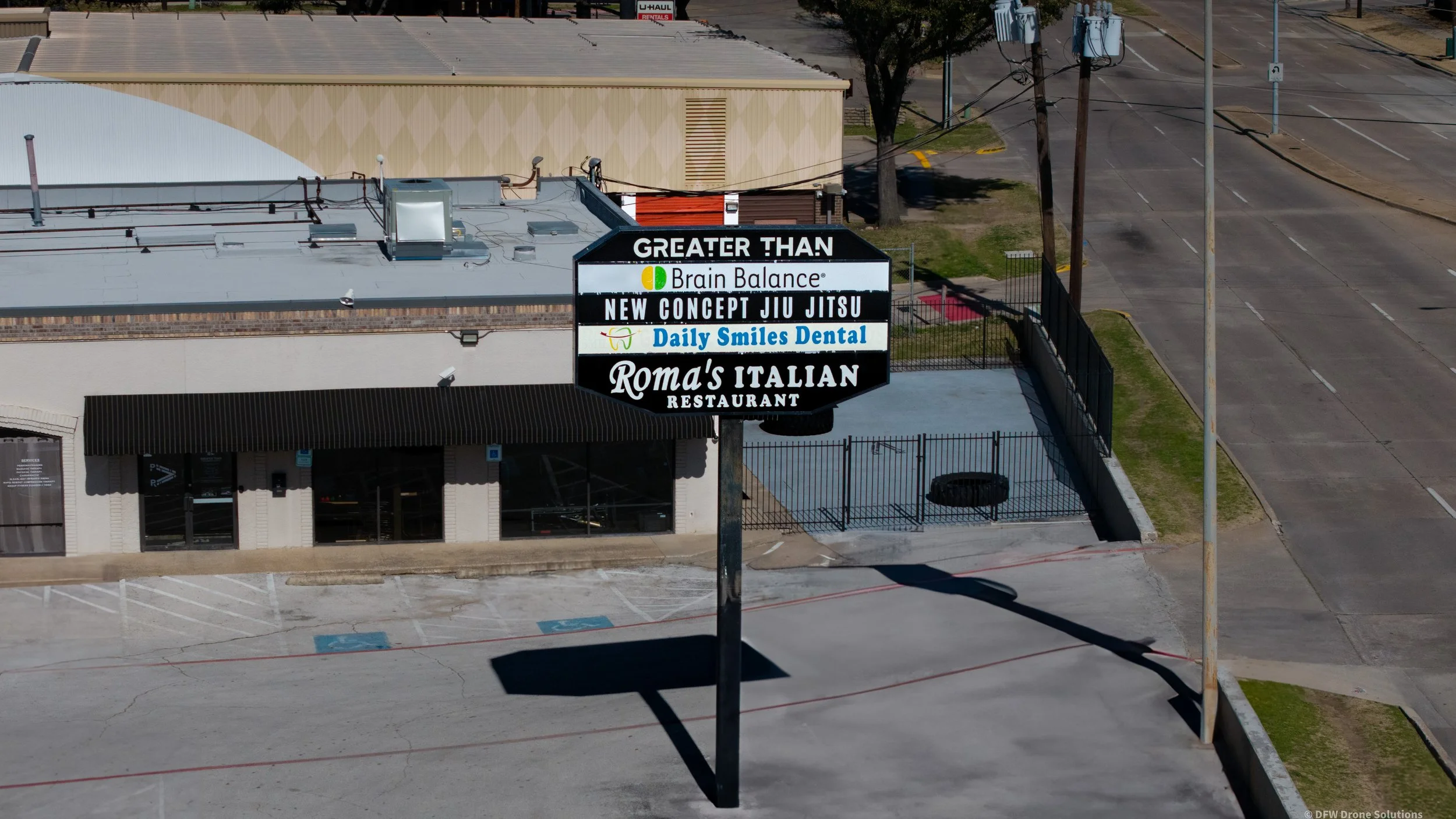 Street view of a commercial building with signs for "Greater Than," "Brain Balance," "New Concept Jiu Jitsu," "Daily Smiles Dental," and "Roma's Italian Restaurant."