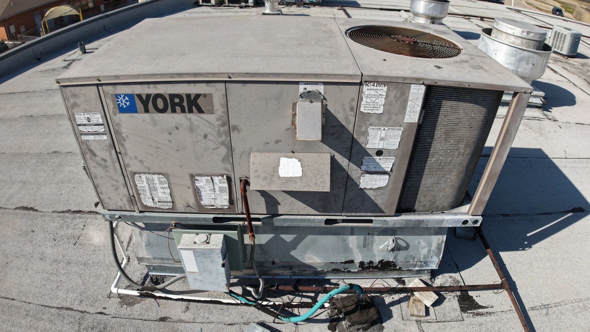 Rooftop air conditioning unit with York branding and various labels, installed on a flat rooftop. It includes visible coil, fans, and electrical components.