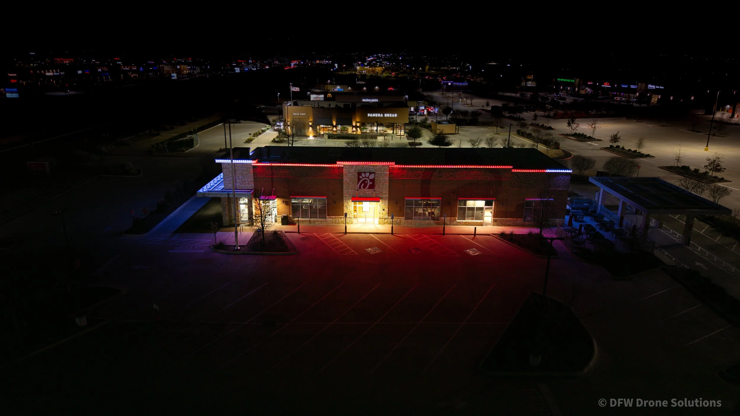 Night aerial view of a restaurant with illuminated signage and surrounding parking lot.