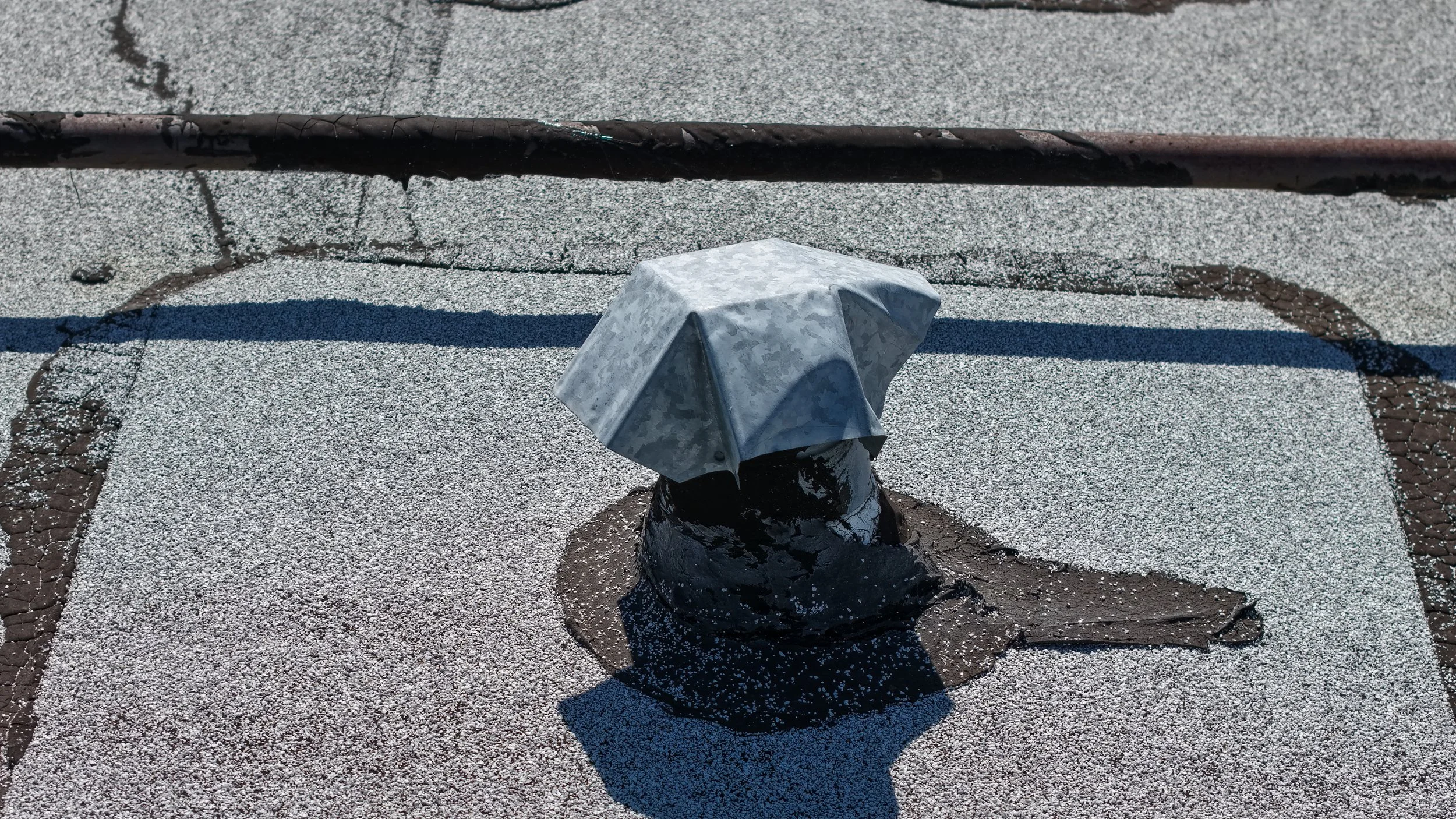 Metal roof vent covered in tar on flat roofing surface