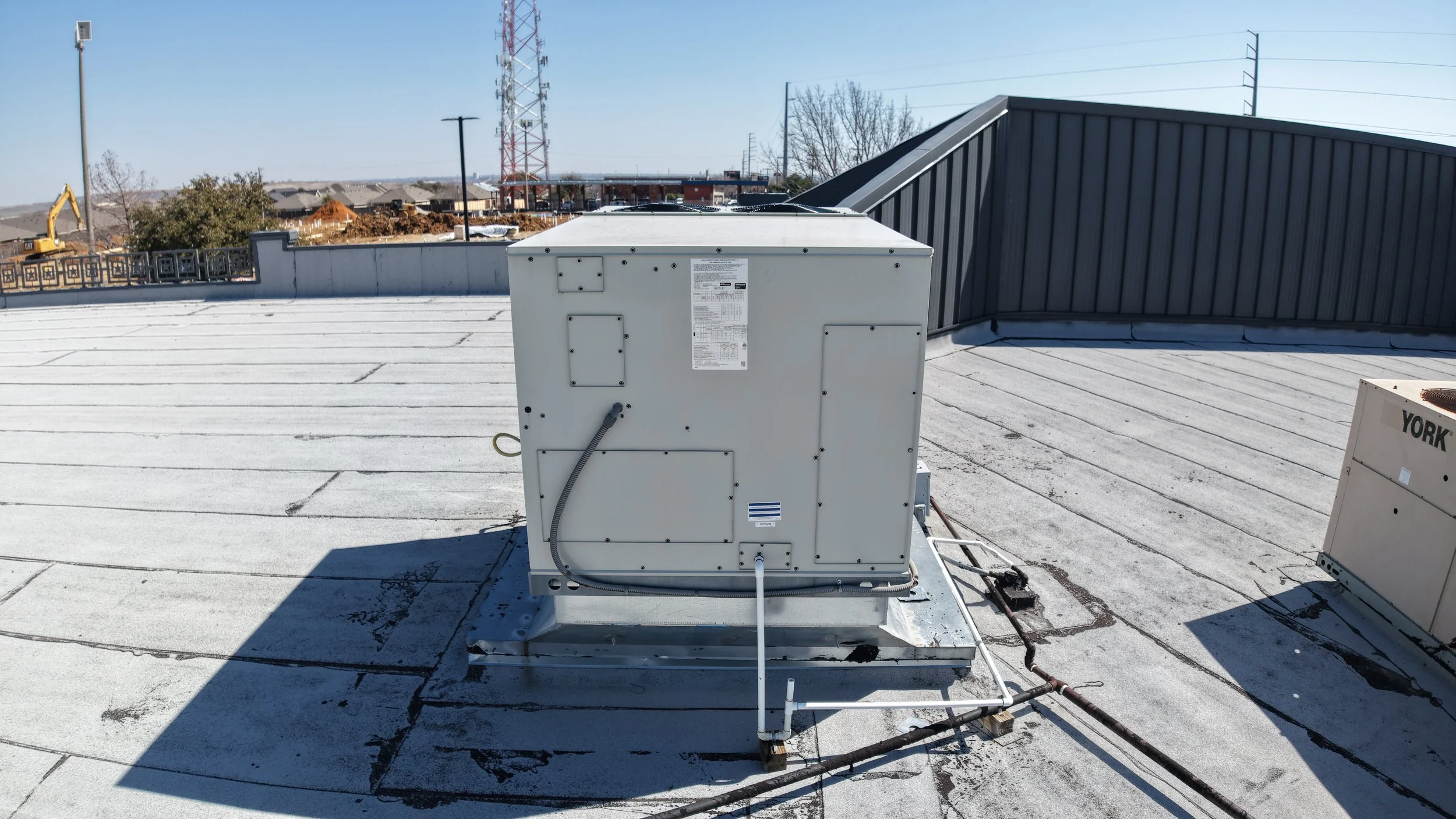 Rooftop HVAC unit on a flat surface with construction equipment and radio tower in background.