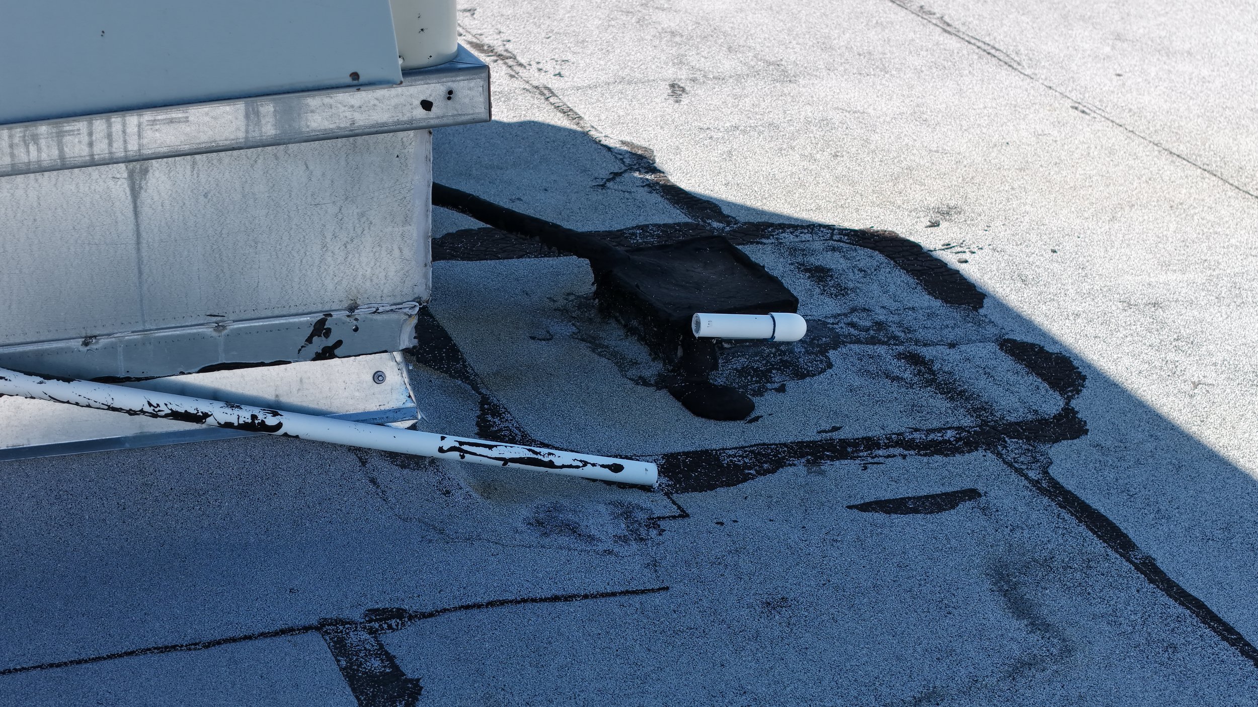Rooftop with metal vent and white pipes on a flat, gravel-covered surface.