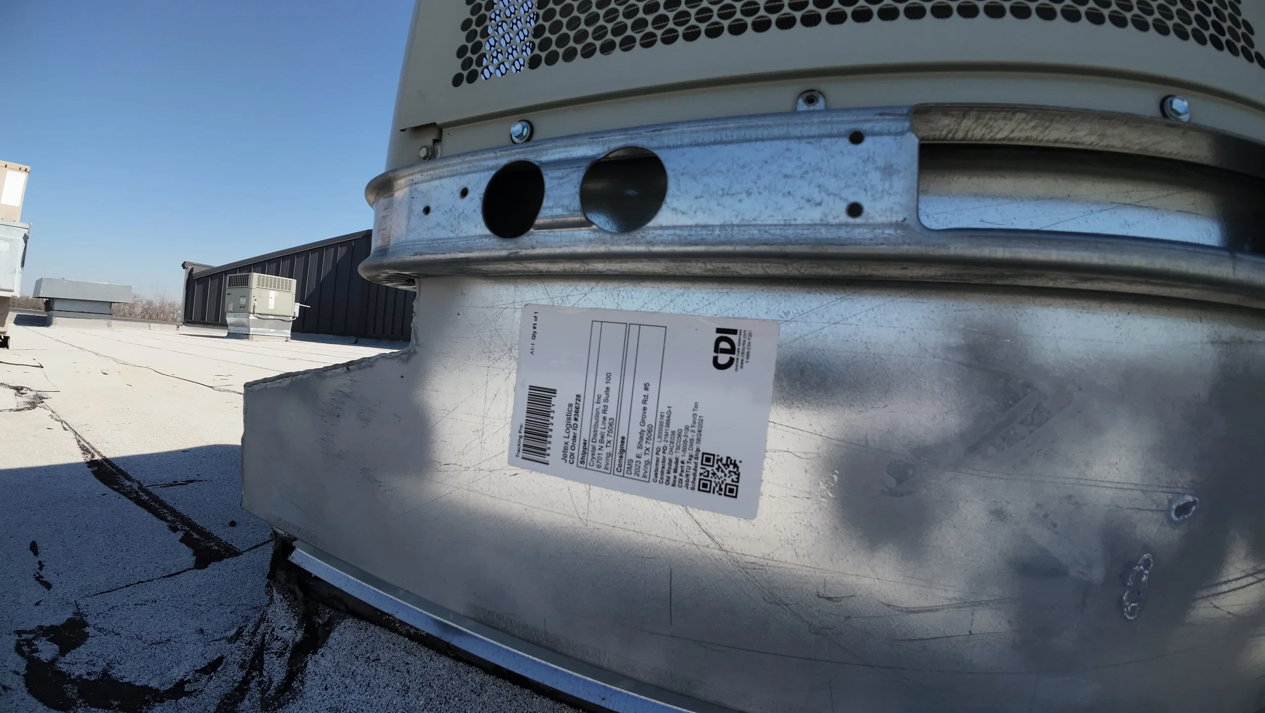 Metal HVAC ductwork on a rooftop with a label, surrounded by ventilation equipment.