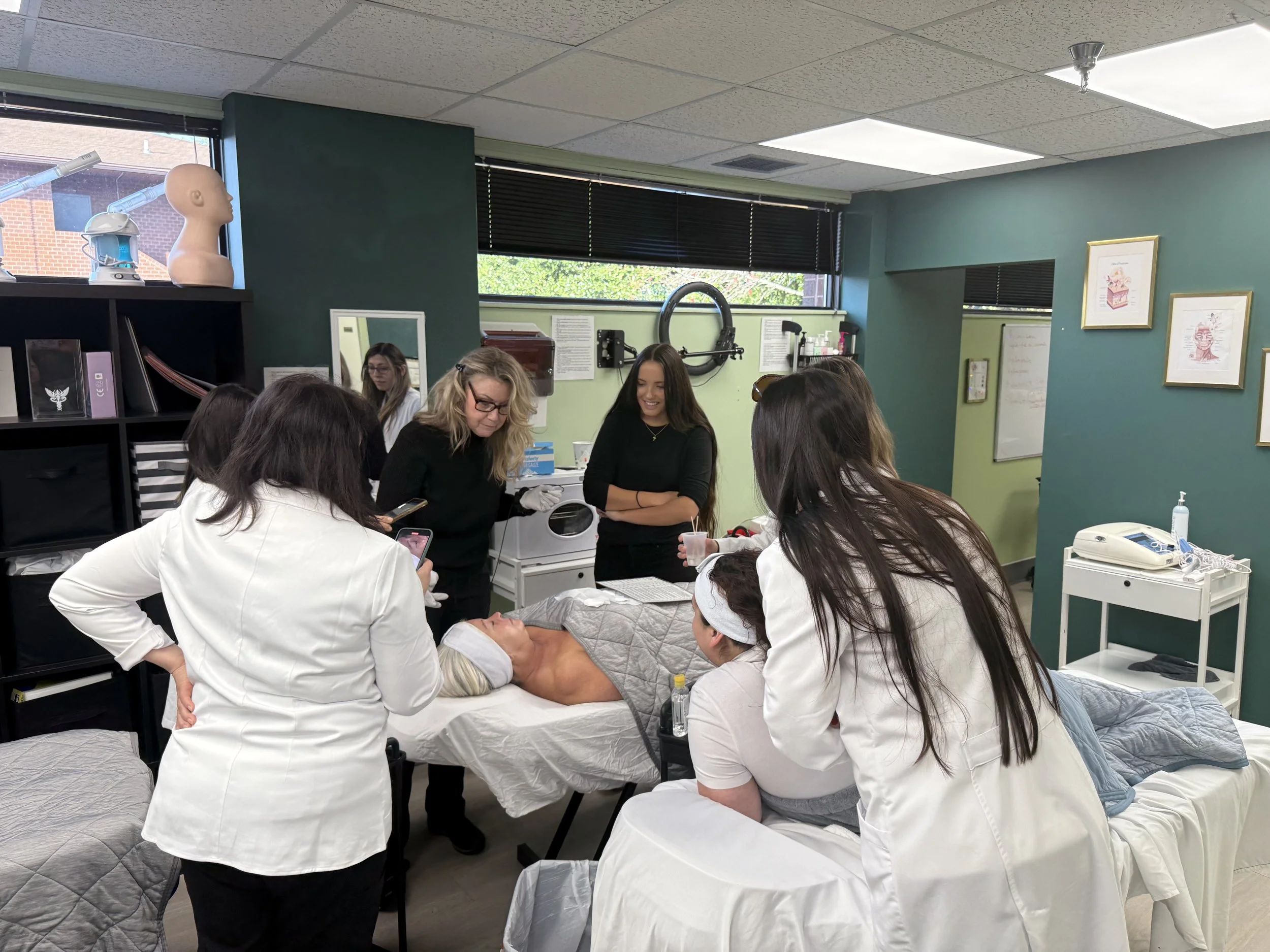 A group of medical professionals gathered around a patient lying on a hospital bed during a demonstration or training session in a clinical room.