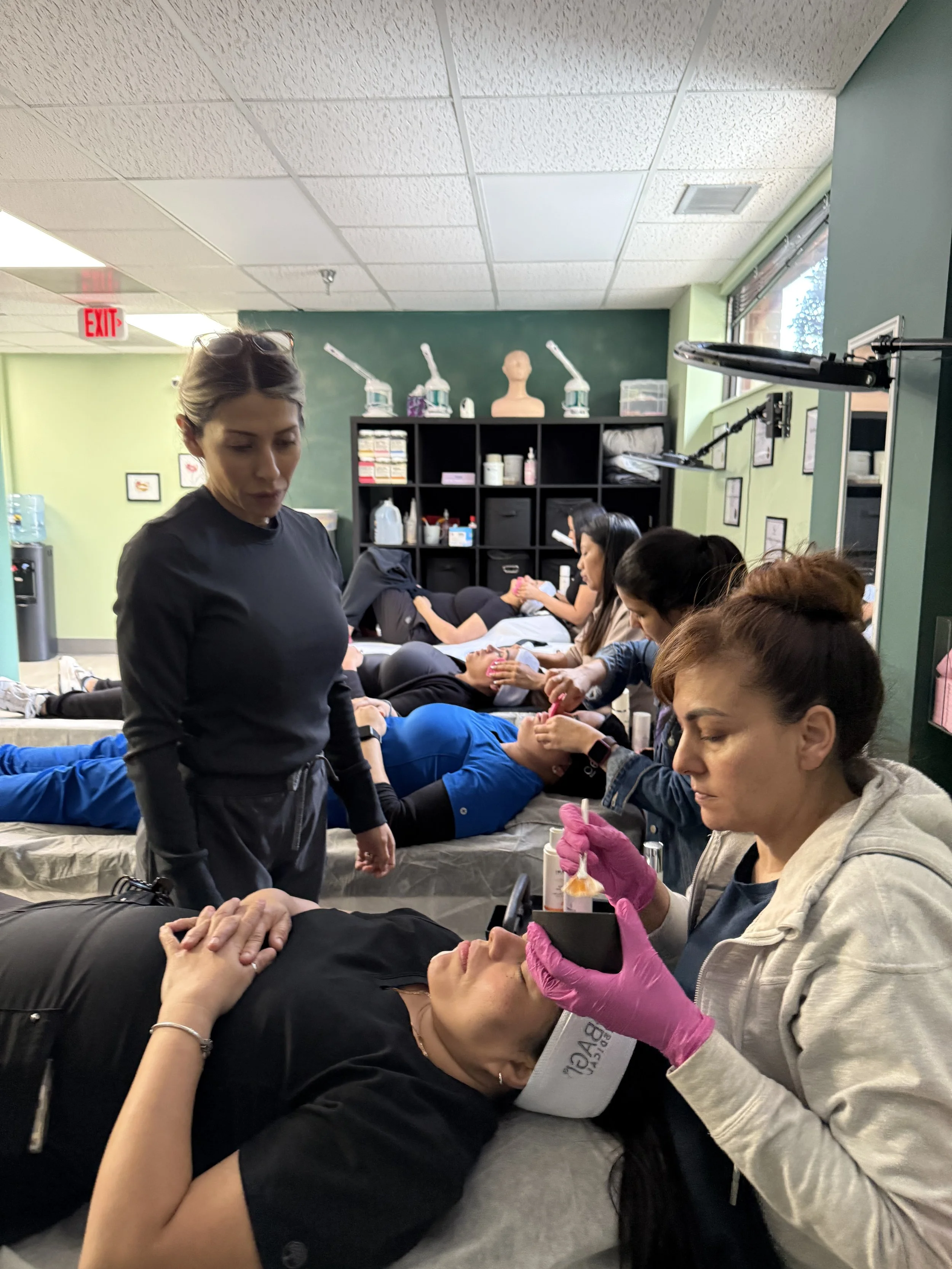 Multiple people receiving eyelash extensions in a beauty salon, with a technician applying extensions to a seated client.