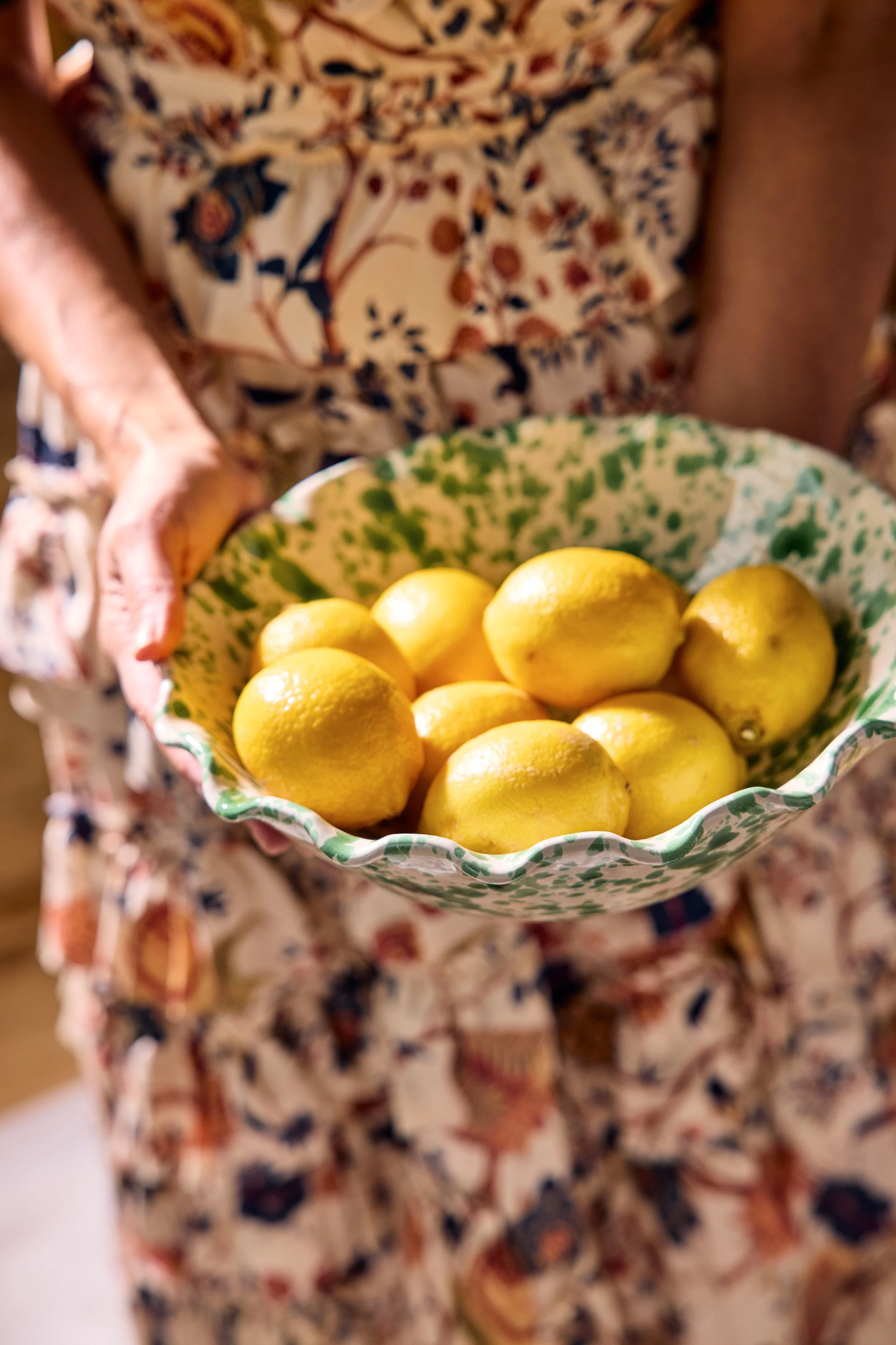 Person holding a bowl of fresh lemons, wearing a floral dress.