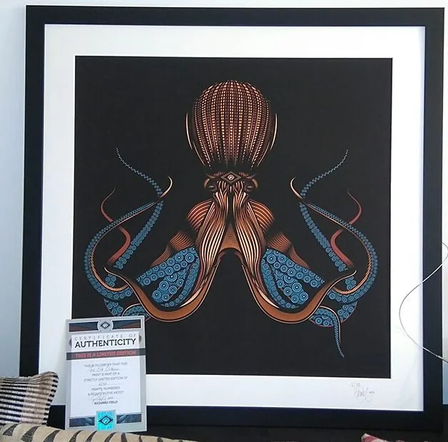 A framed artwork of a stylized octopus with intricate patterns, mainly in brown, blue, and orange, on a black background.