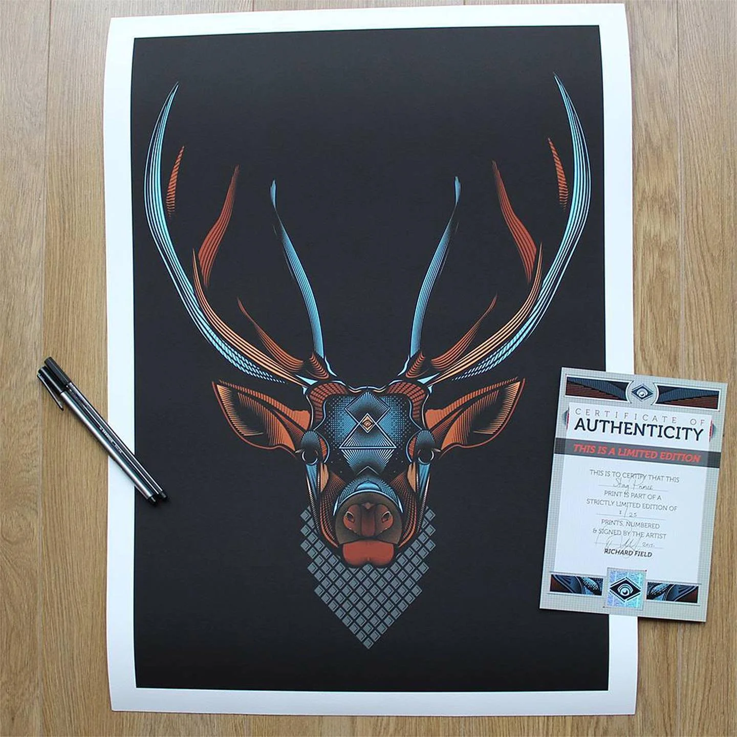 Colorful digital artwork of a deer's head with antlers, on a black background, next to a certificate of authenticity and a black pen.