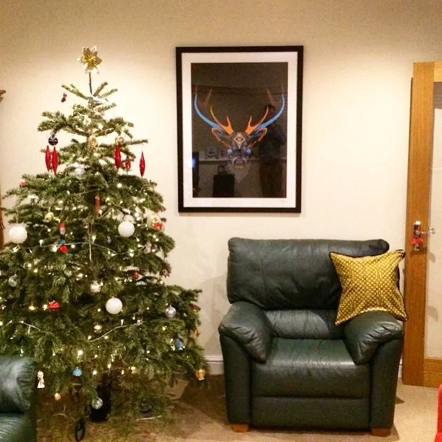 Living room corner with decorated Christmas tree, framed deer artwork, and a green leather armchair with a yellow pillow.