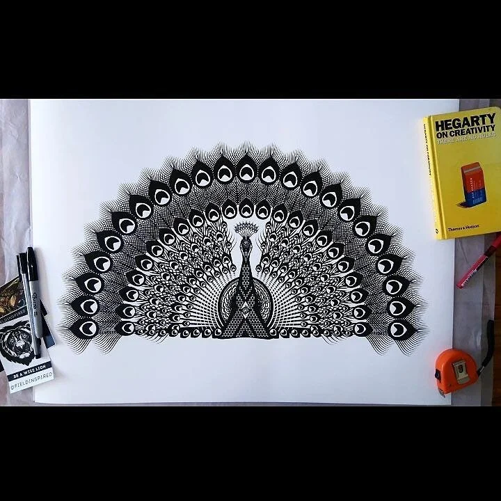 Intricate black and white drawing of a peacock with its feathers fanned out, created on a large white sheet of paper.