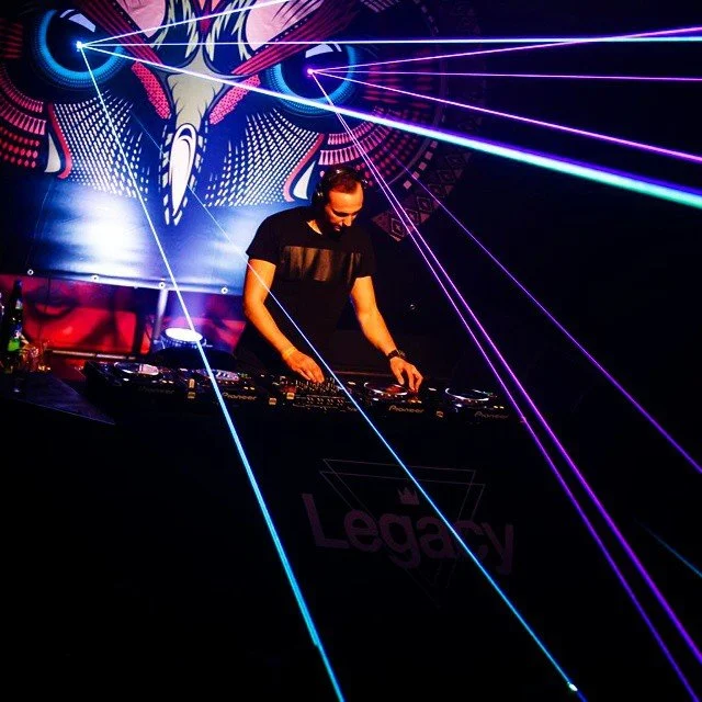 DJ performing at a nightclub with colorful laser lights and a vibrant backdrop