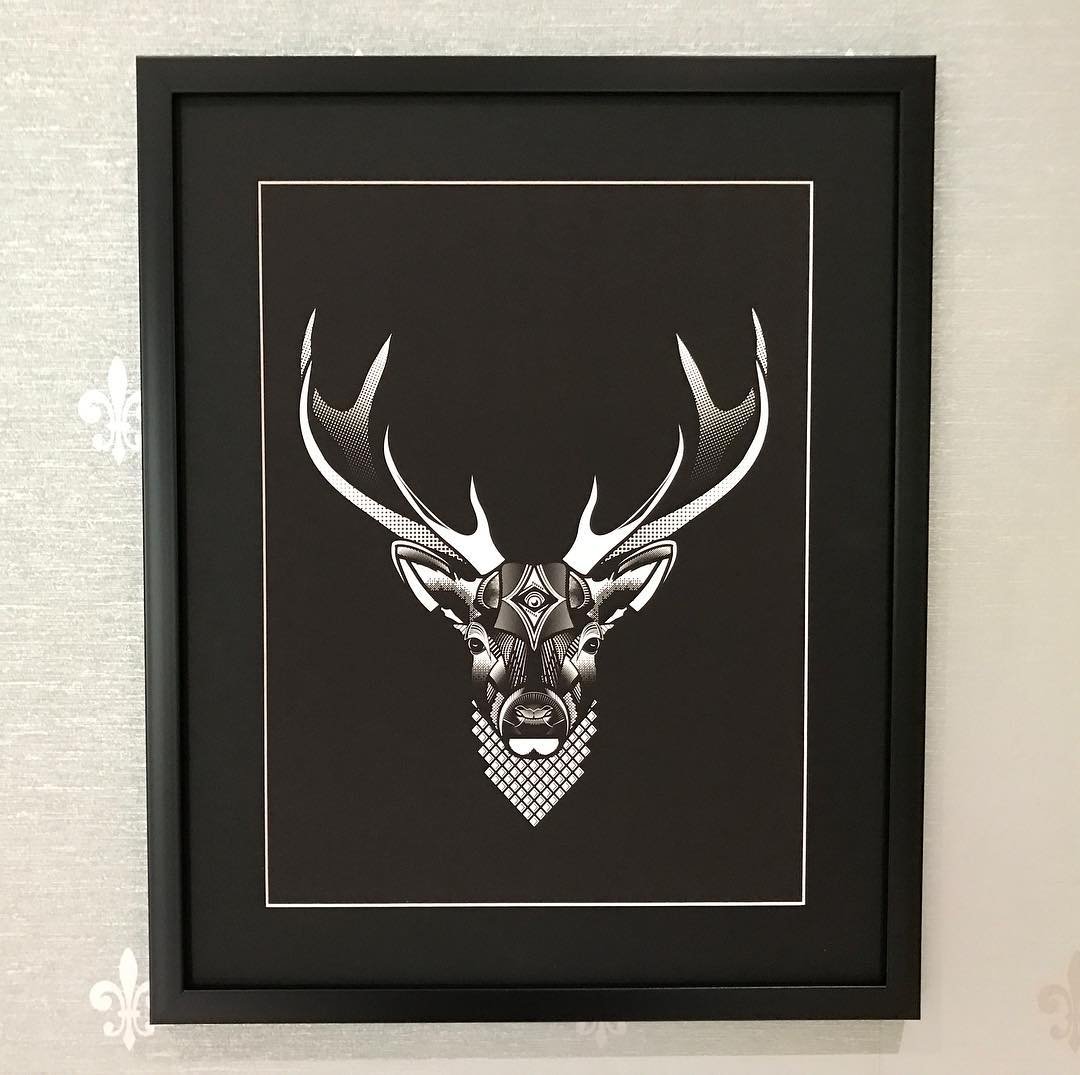 Framed black and white geometric illustration of a deer's head with large antlers on a light-colored wall.