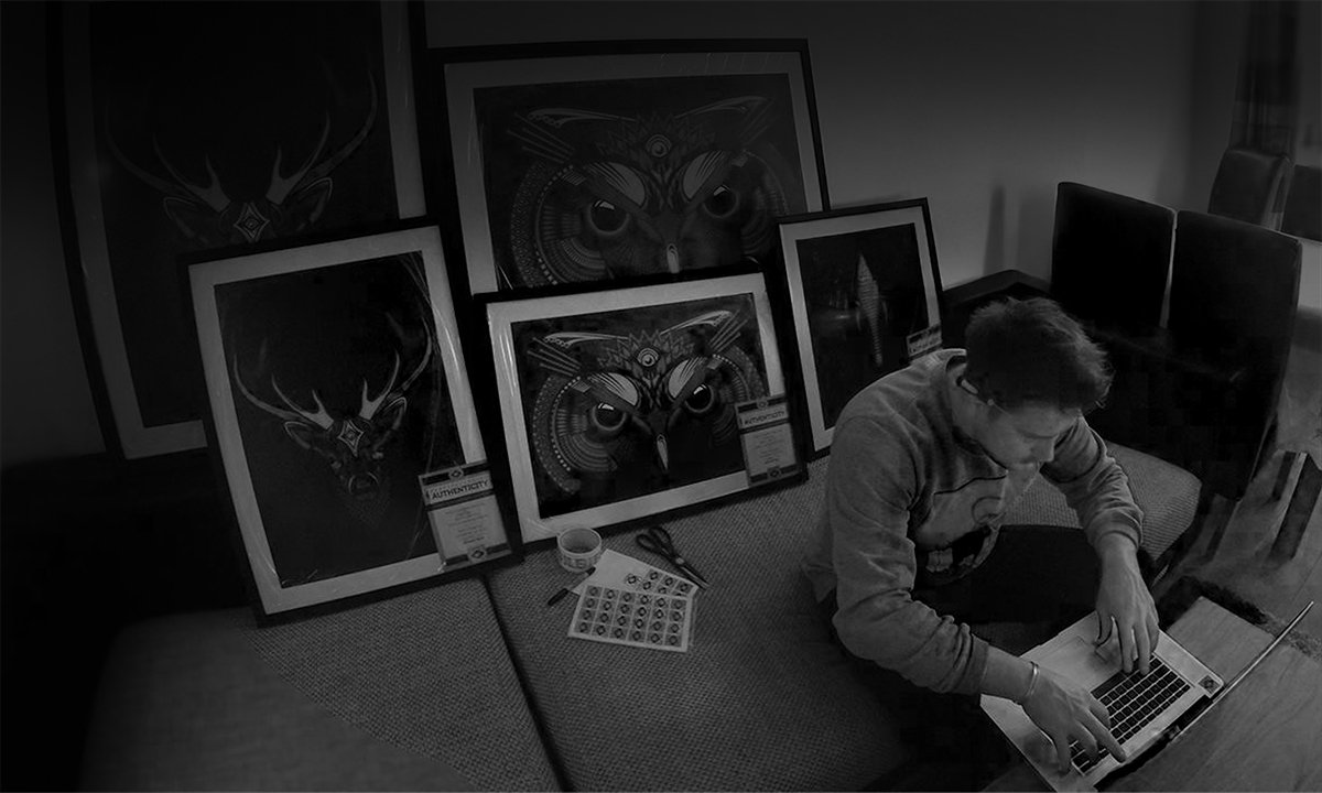Rich Field Fieldinspired working on a laptop at a table with framed artwork of the dark owl and King Stag designs leaning against the wall in the background.