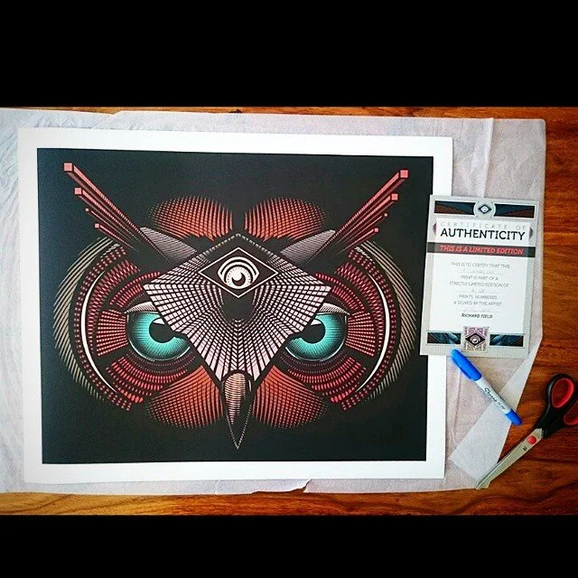 Digital artwork of an owl with prominent detailed eyes and geometric patterns, placed on a wooden surface with a certificate of authenticity, scissors, and a marker nearby.