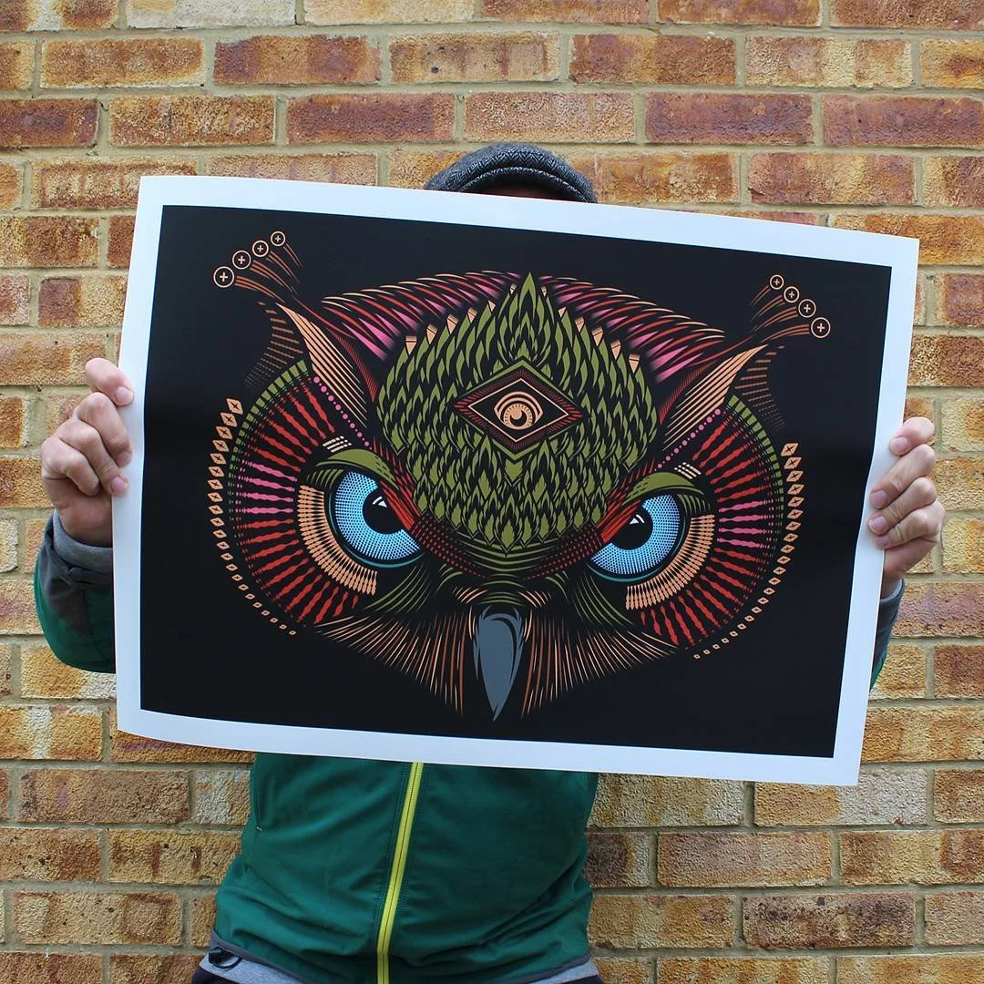 Person holding a colorful, stylized owl illustration in front of a brick wall.