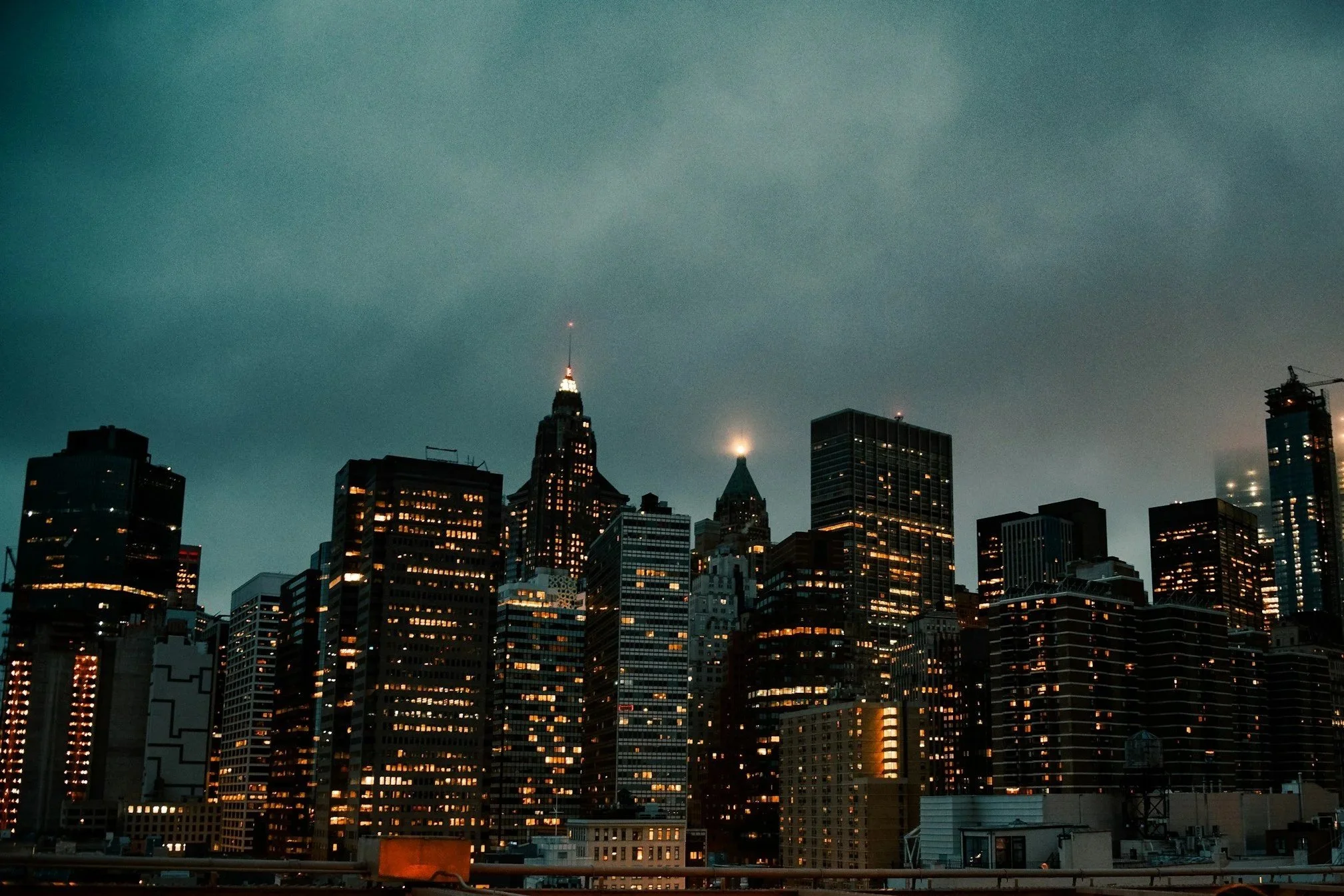 Nighttime city skyline of New York City with illuminated skyscrapers and Empire State Building in the background.