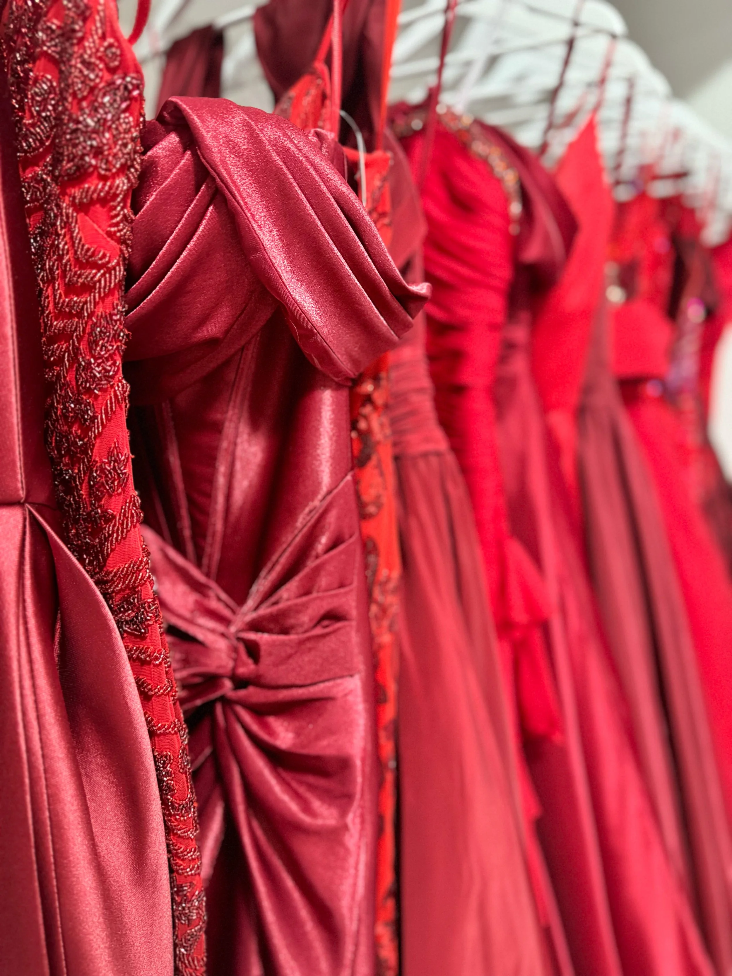 Vivid red dresses with various textures and embellishments hanging on a rack.