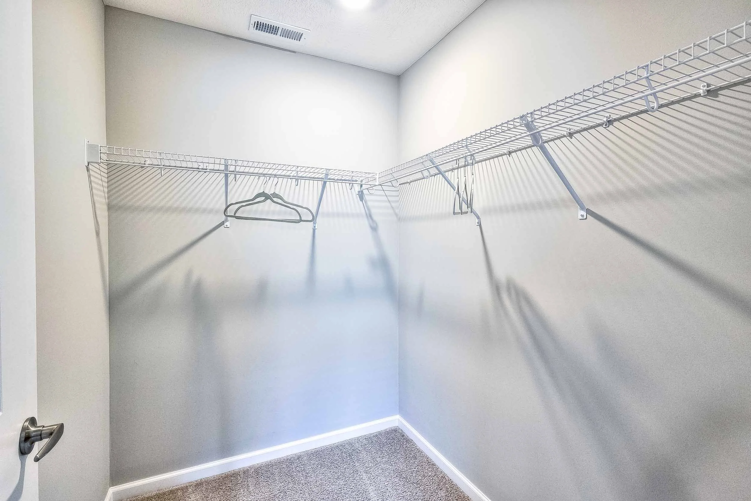 Empty walk-in closet with white wire shelving and a few empty hangers, beige carpet, and white walls.