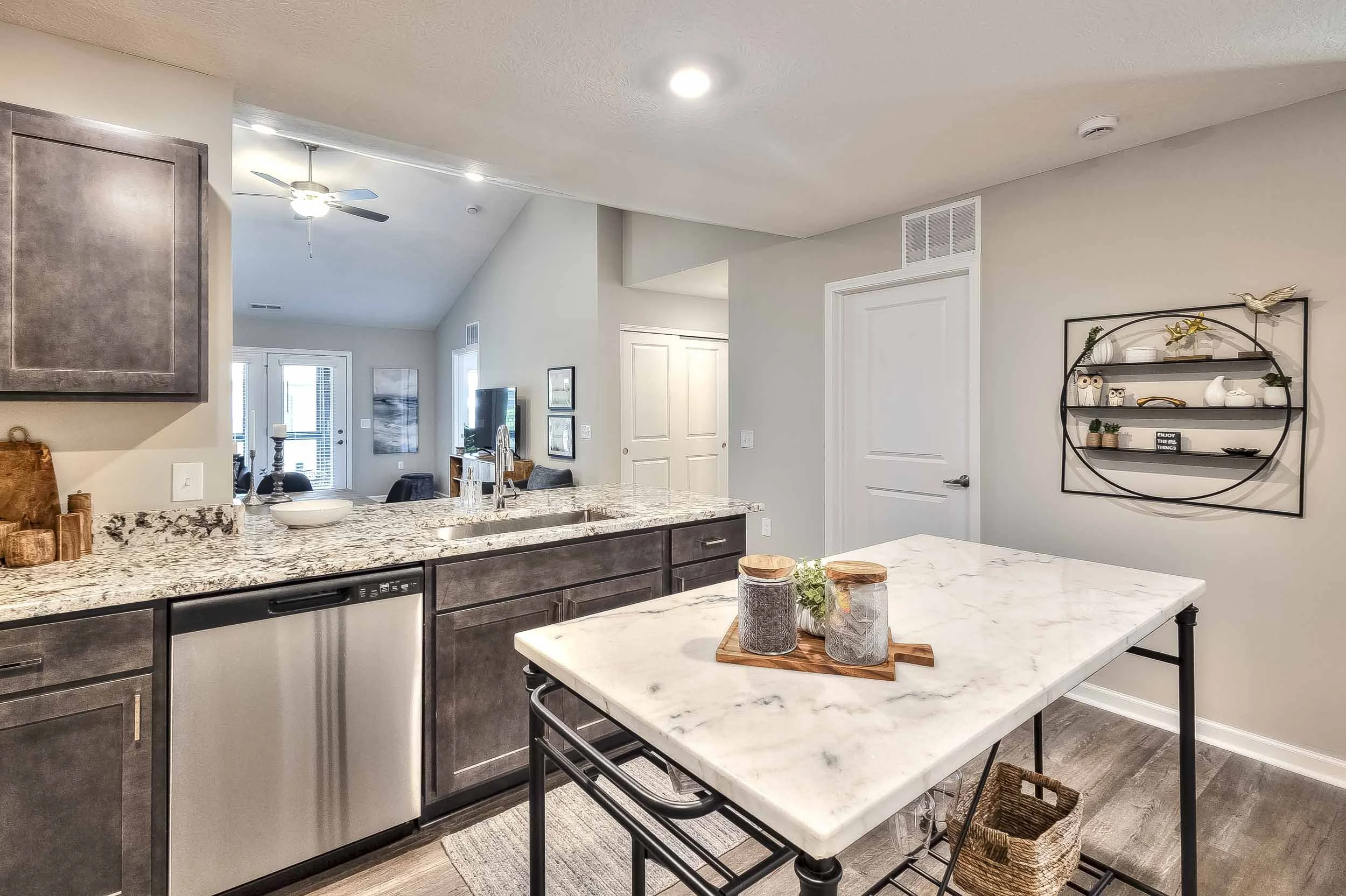 Kitchen with granite countertops, gray cabinets, and a small marble dining table, opening to living area with a TV and glass door to outdoor space.