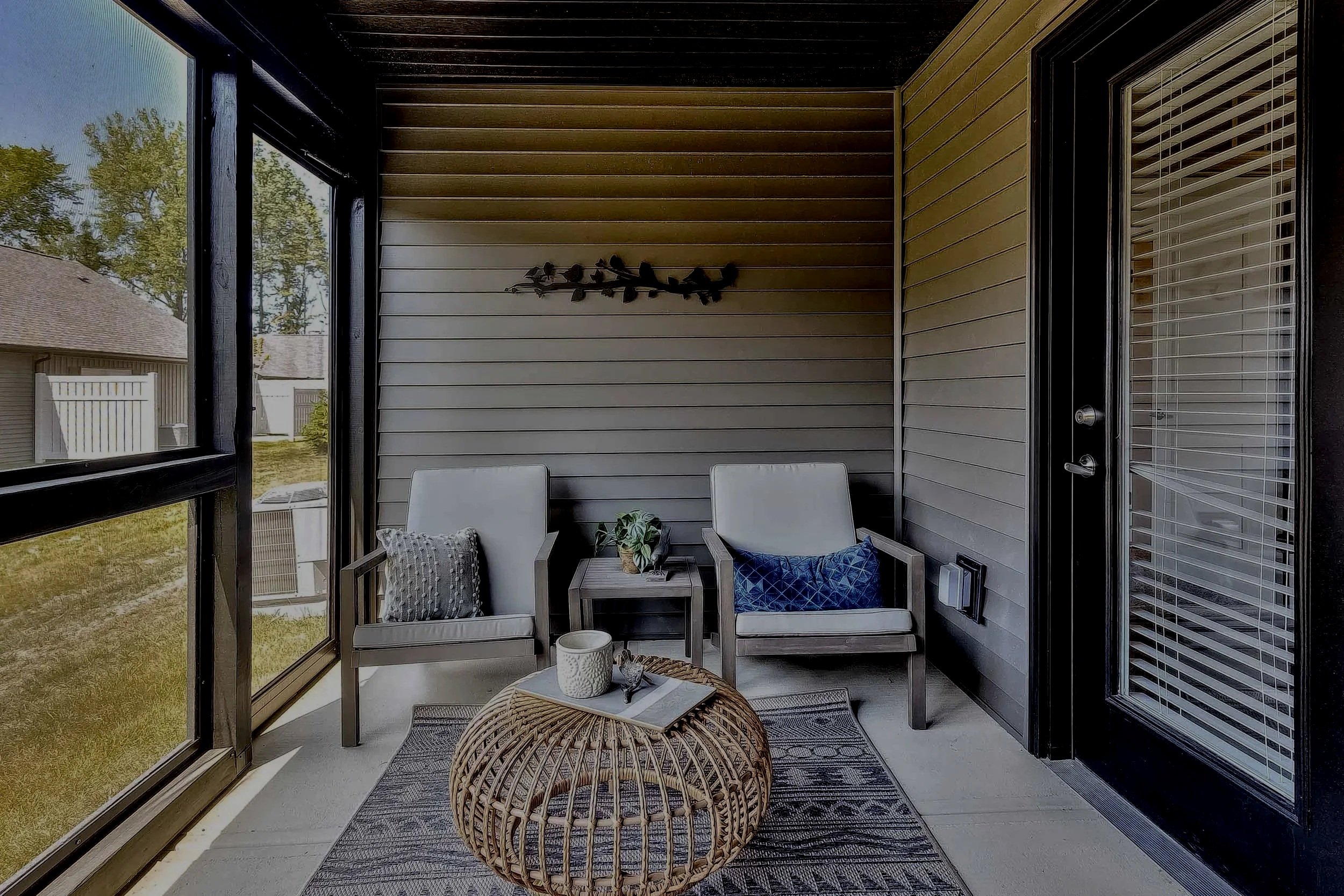 Home rental back patio with screened-in porch. Two cushioned outdoor chairs sit around a rug and fancy wicker coffee table.