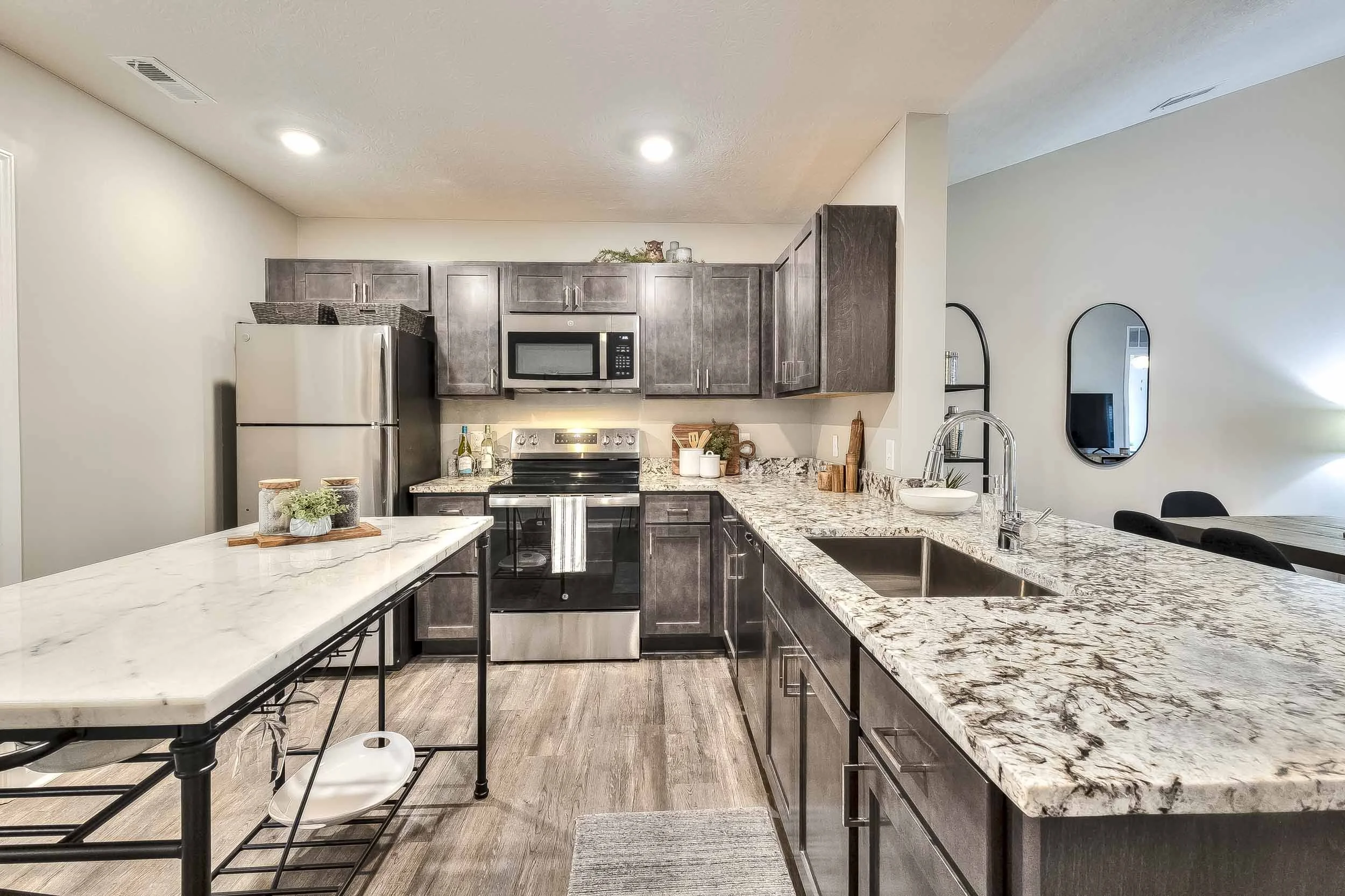 Modern kitchen with granite countertops, dark wood cabinets, stainless steel appliances, and a small island with plants.