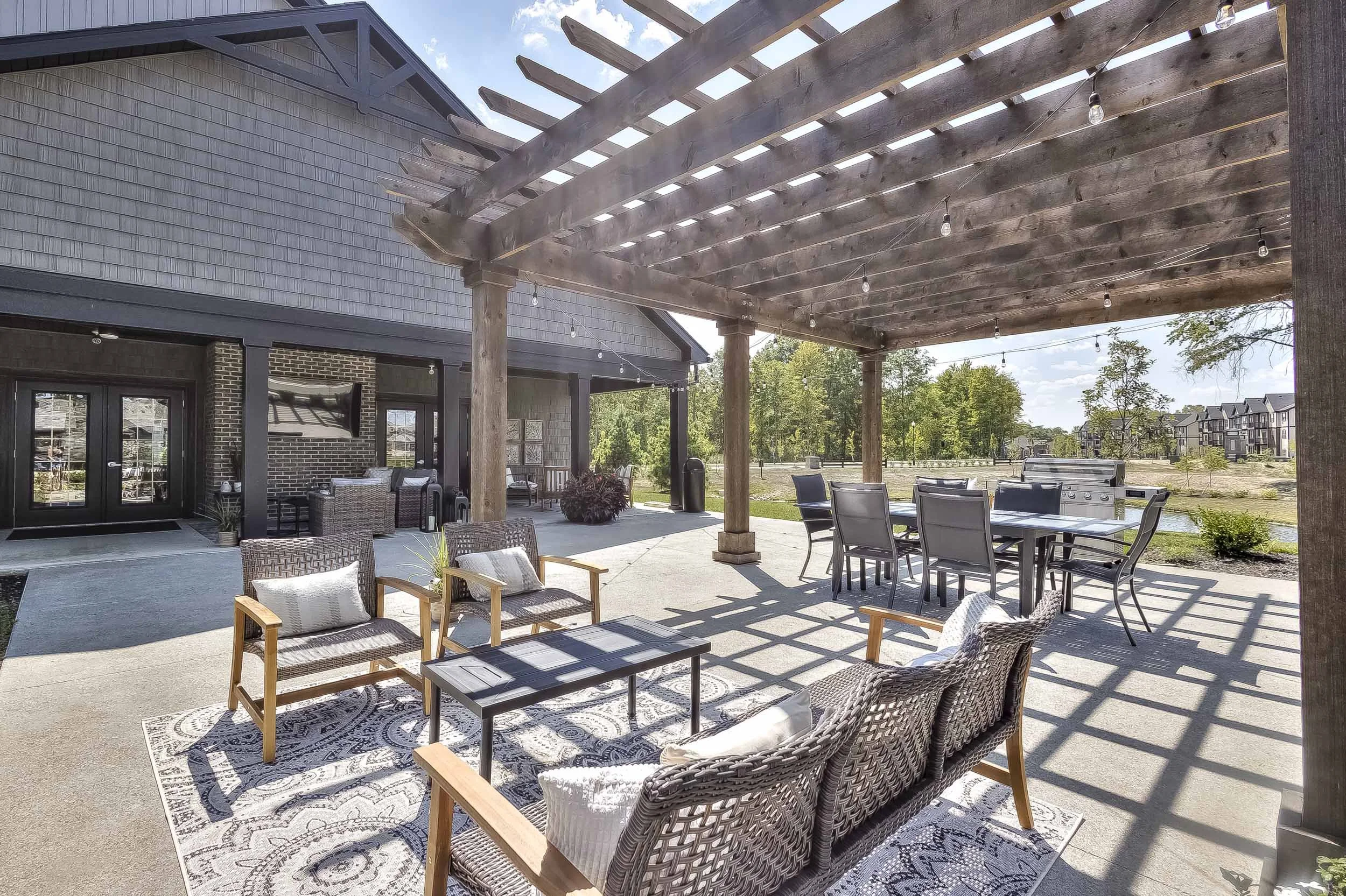 Outdoor patio with seating area, wooden pergola with string lights, and a view of a pond and houses in the distance.