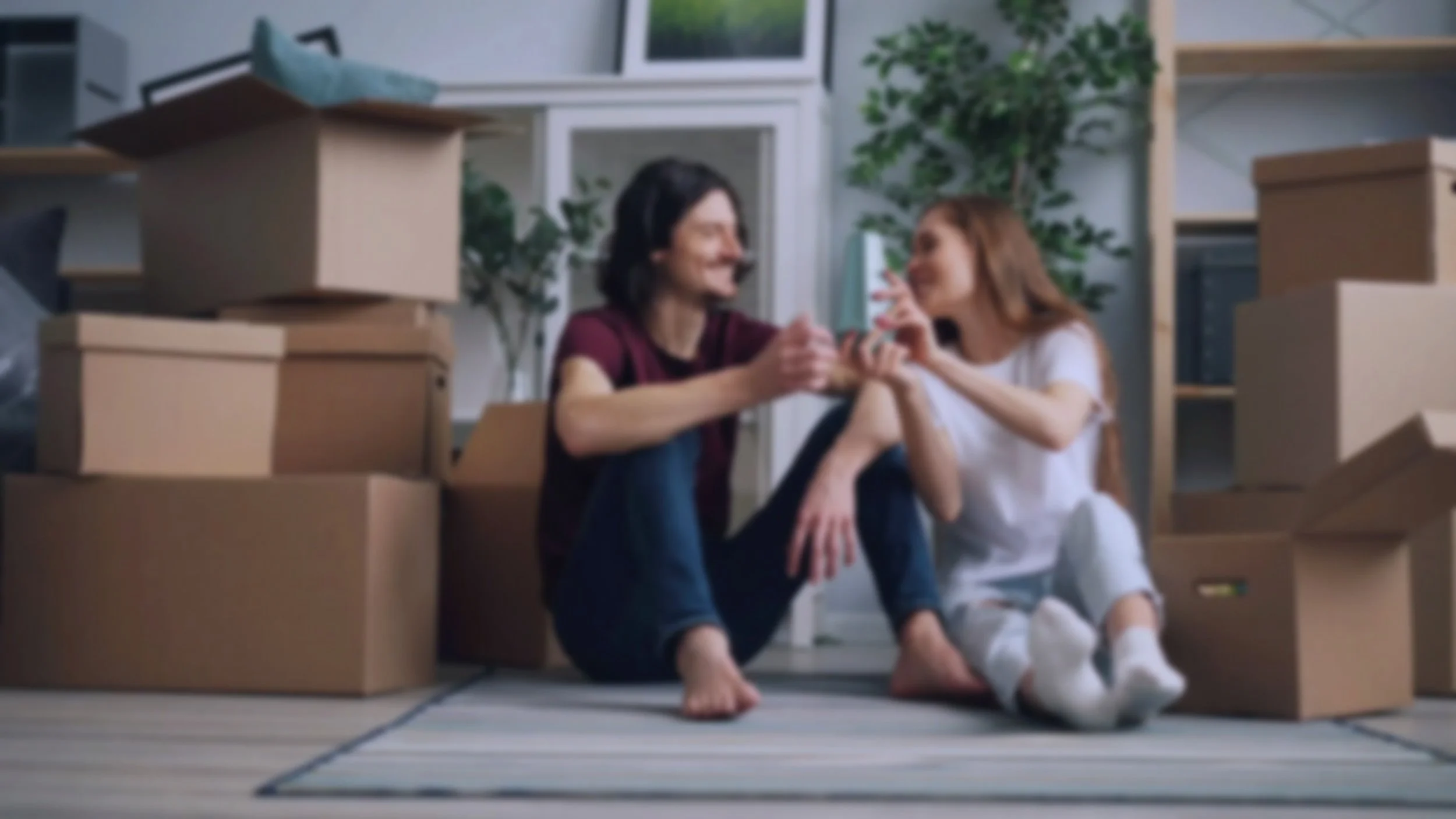 A woman and a girl sitting on the floor surrounded by moving boxes, sharing a tender moment in a new home.