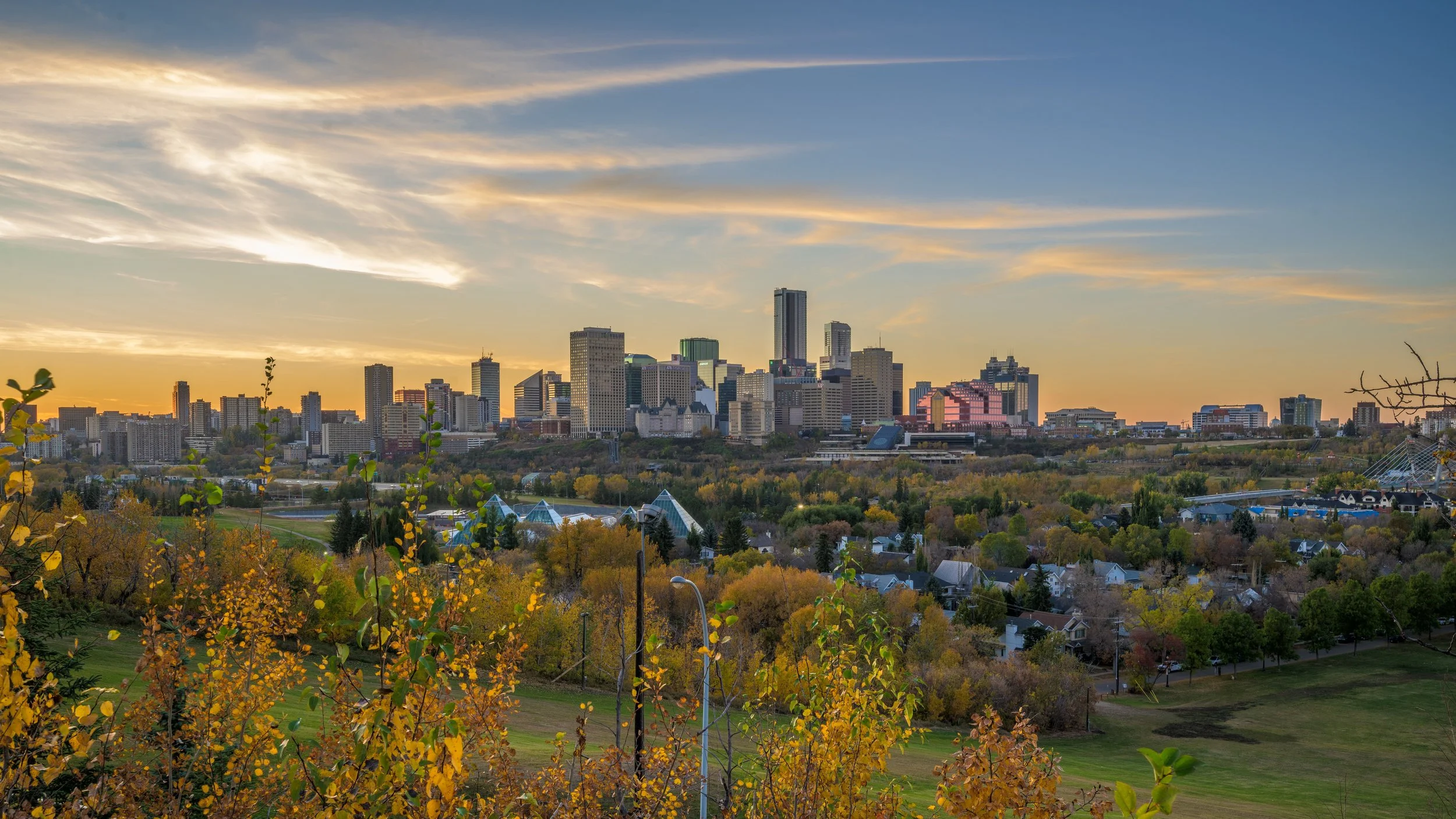 City skyline at sunset with a mix of tall buildings and trees in the foreground