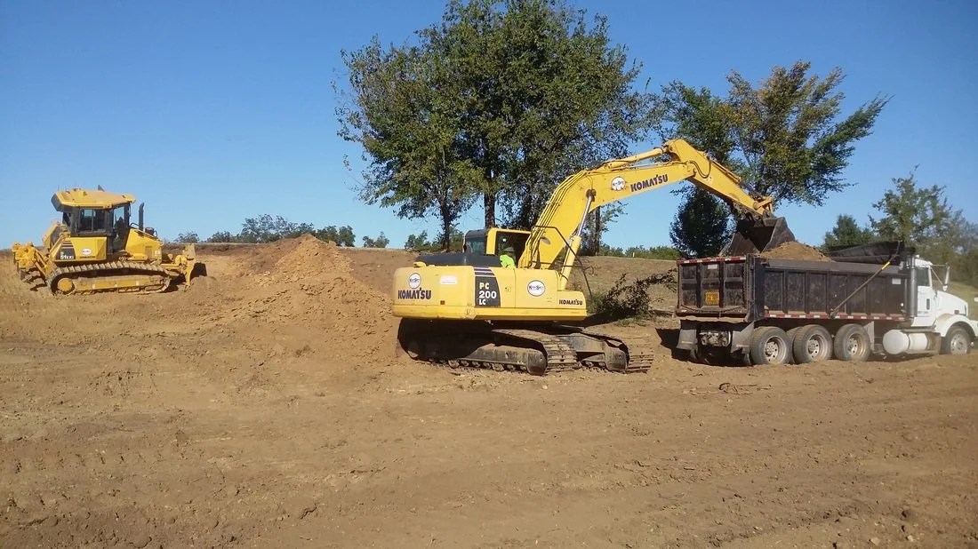 Excavator loading excavated soil into dump trucks for material export.