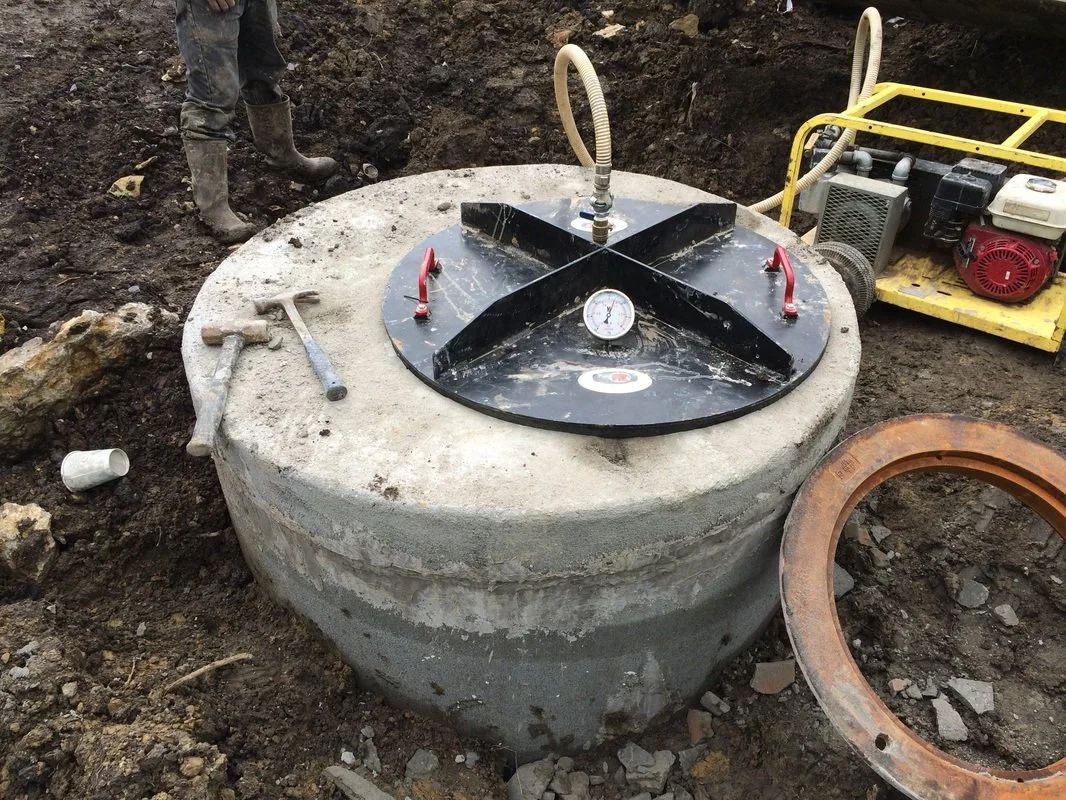Sanitary sewer manhole installation with concrete structure and sealed access lid at an active job site.