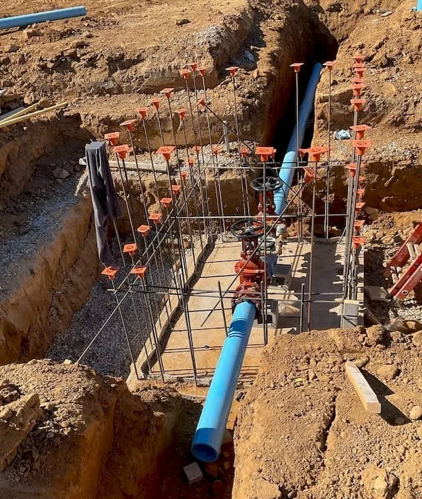 Blue pipe running through a trench, surrounded by metal rebar supports, and a red valve assembly in the center.