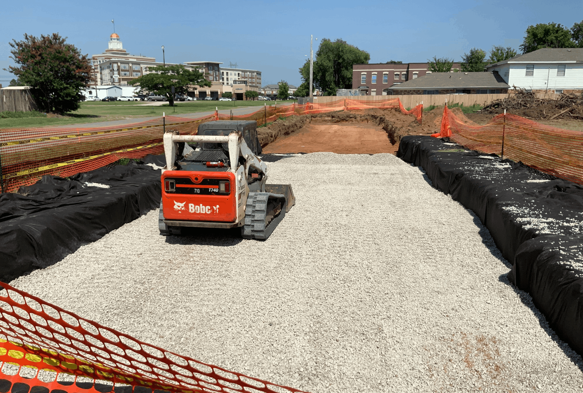 Skid steer spreading aggregate over underground stormwater system