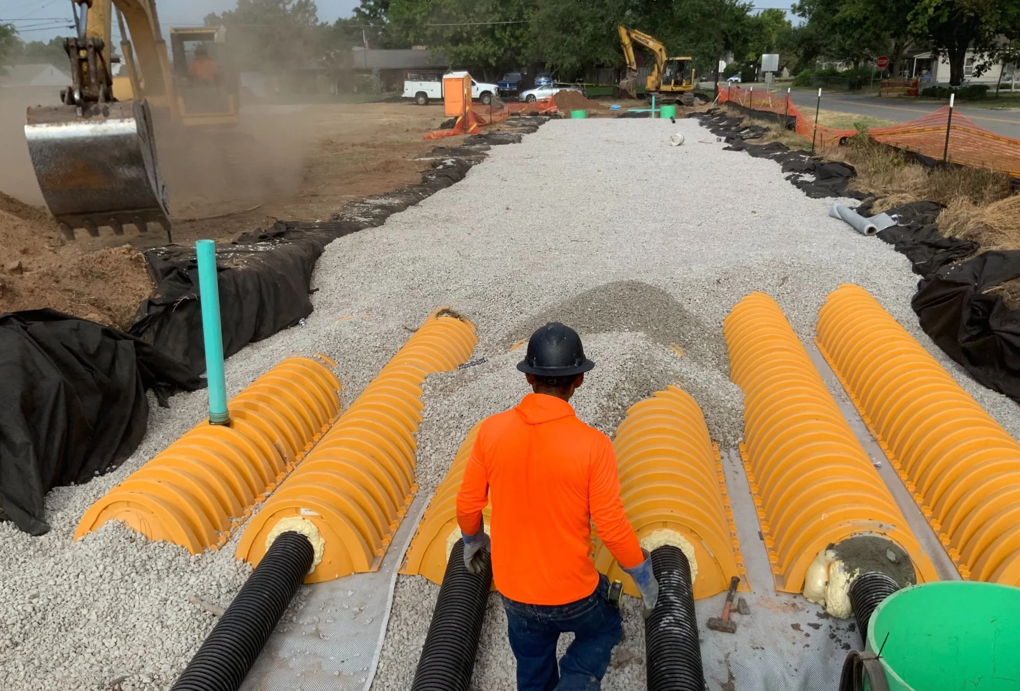 Worker installing underground stormwater chambers with aggregate backfill