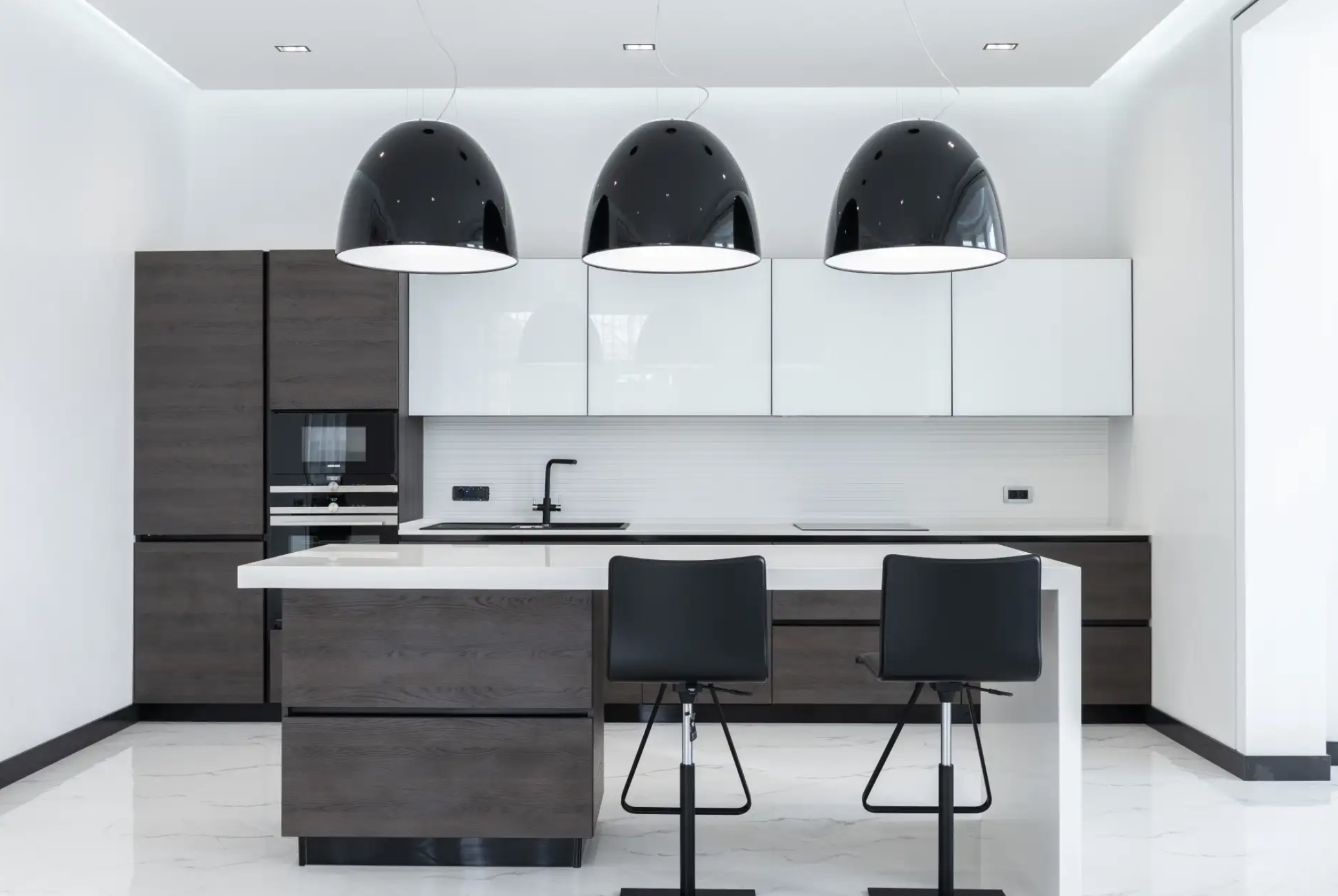 Modern kitchen with black pendant lighting, white cabinets, and a kitchen island with two black chairs.