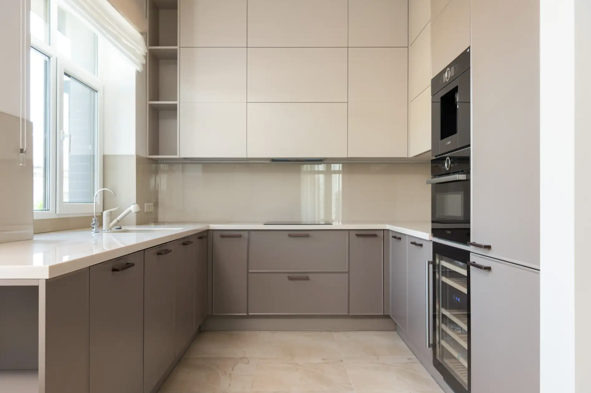 Modern kitchen with beige and gray cabinets, a white countertop, and built-in appliances including a microwave and wine cooler.
