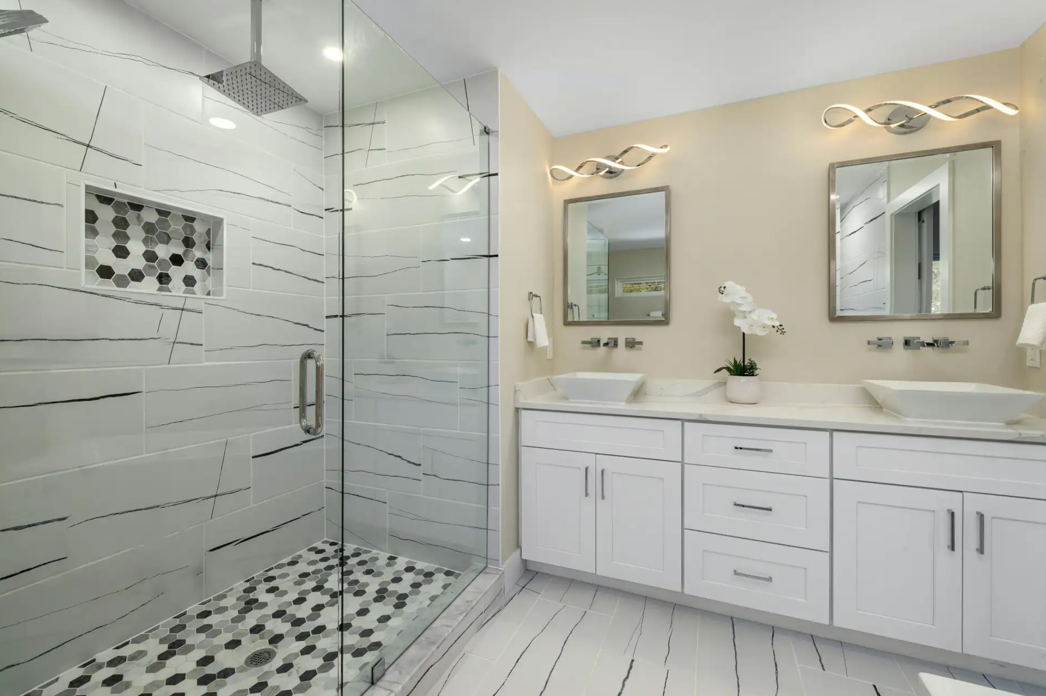 Modern bathroom with glass-enclosed shower, white cabinets, two vessel sinks, round mirrors, and minimalistic decor including a white orchid plant.