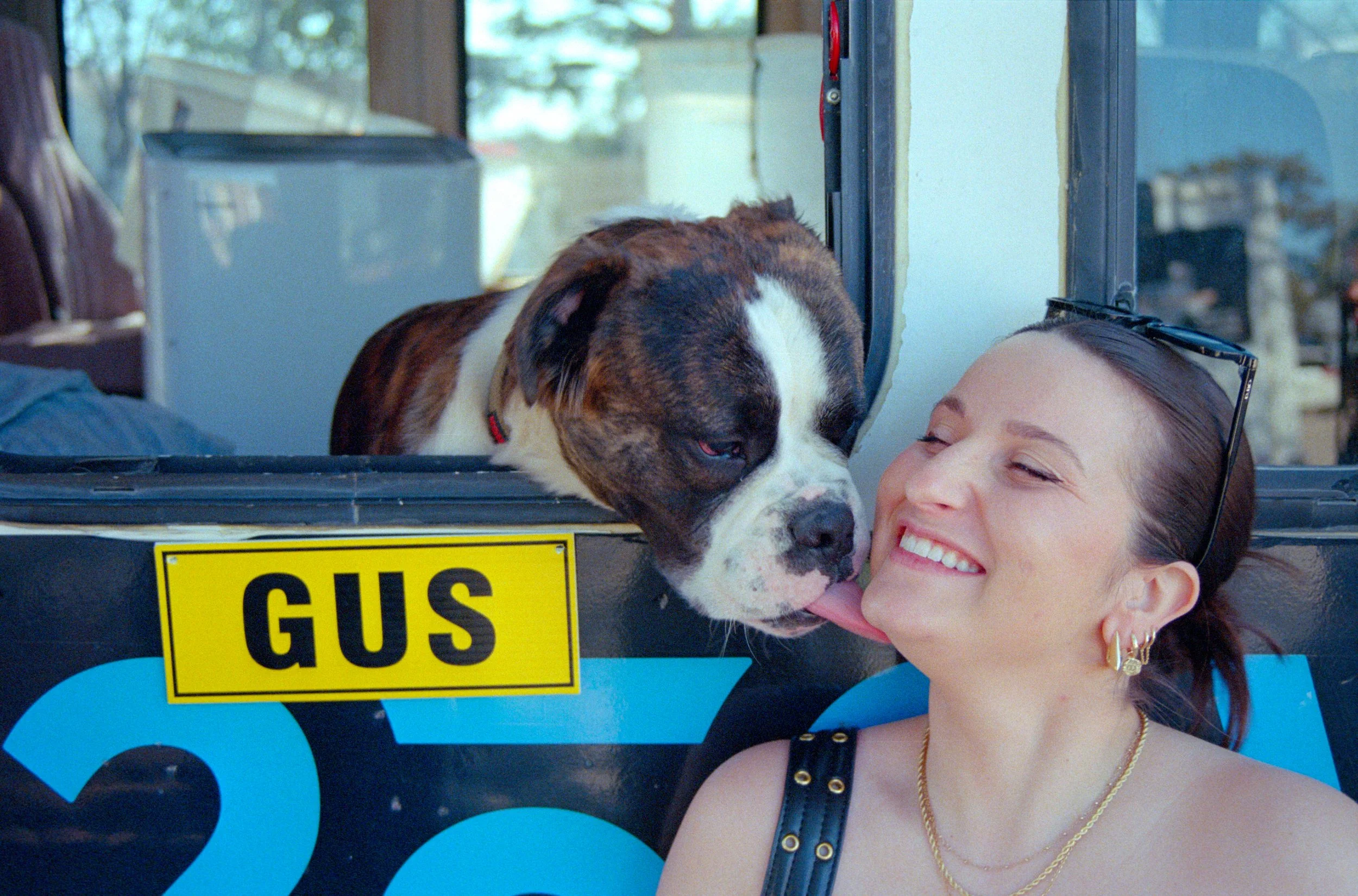 A woman and a dog at a pet grooming or vet station, with the dog licking her face.