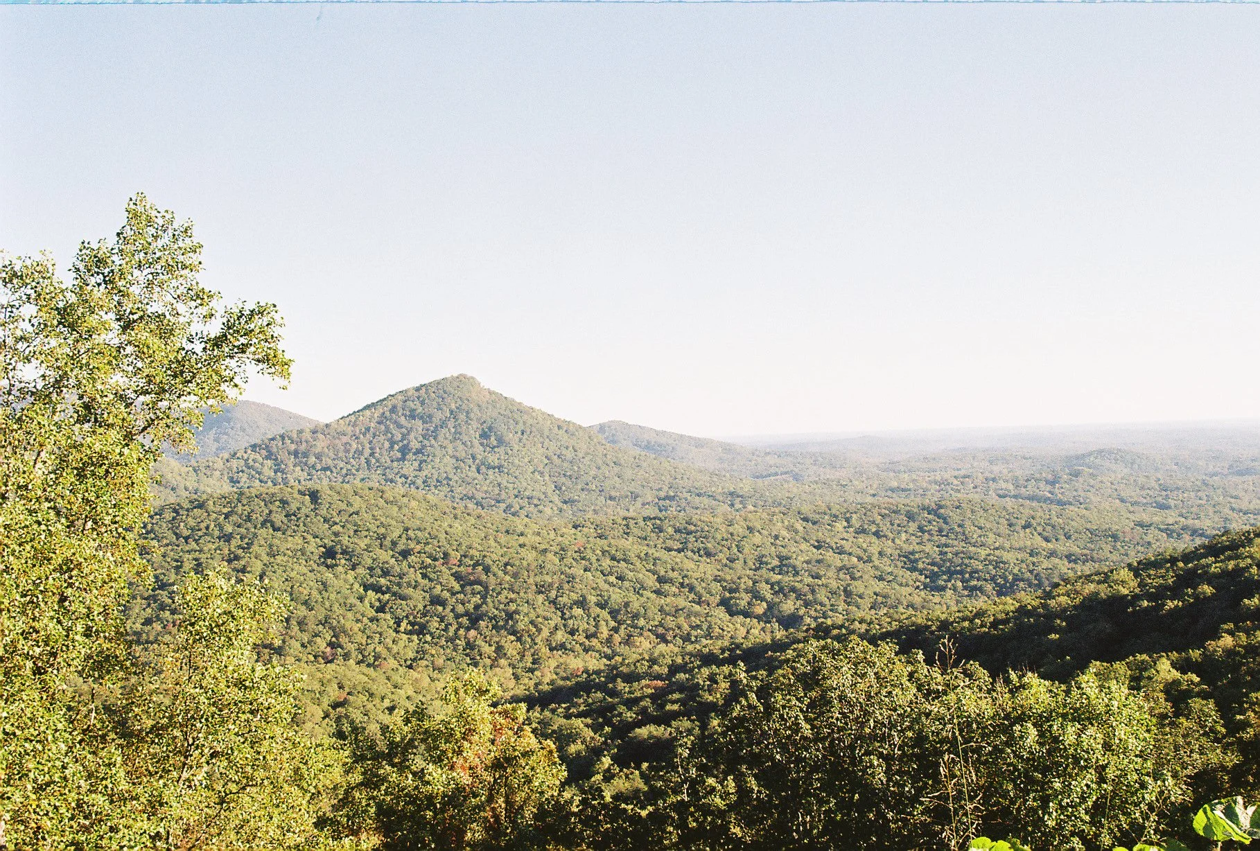 A panoramic view of a lush, green mountain landscape with rolling hills and a clear sky in the background.