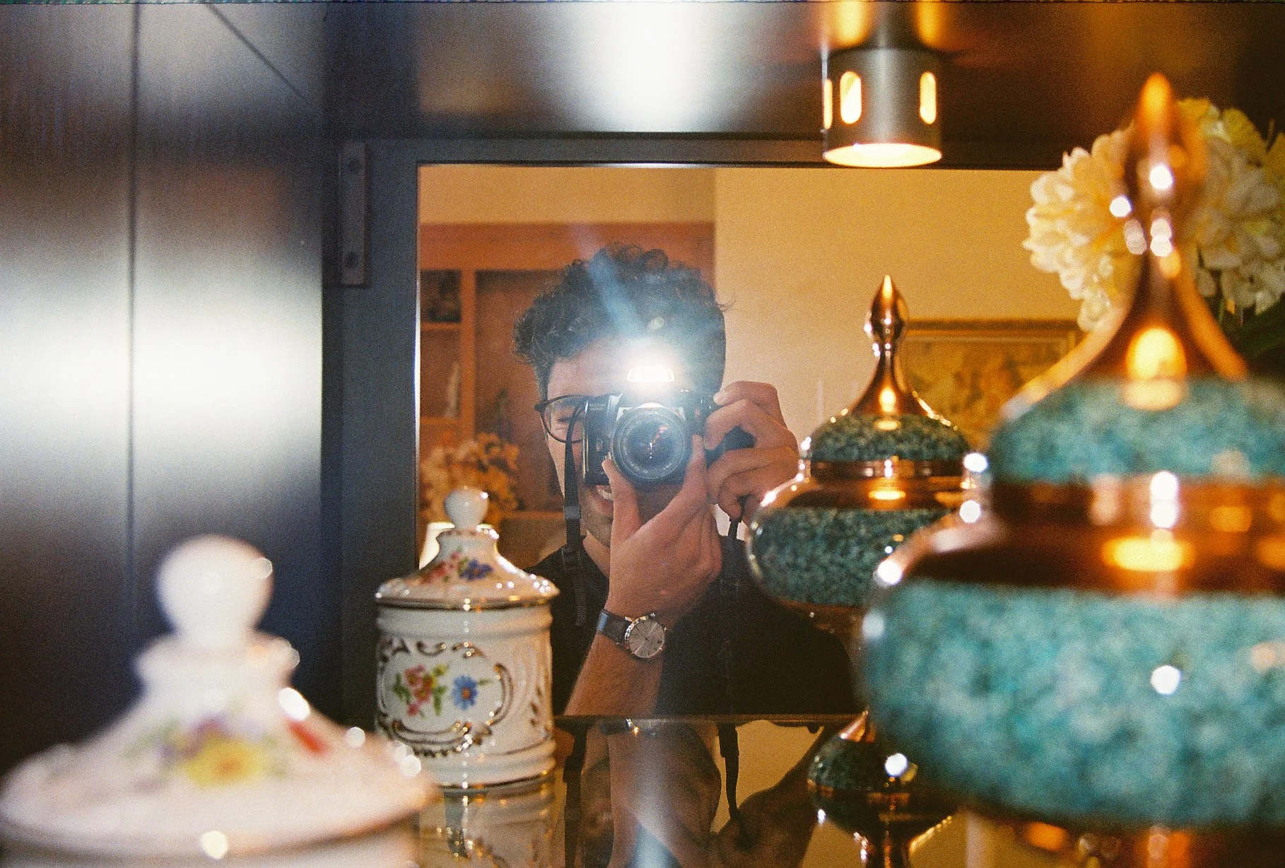A man taking a photo of himself in a mirror, surrounded by decorative ceramic vases and ornaments.