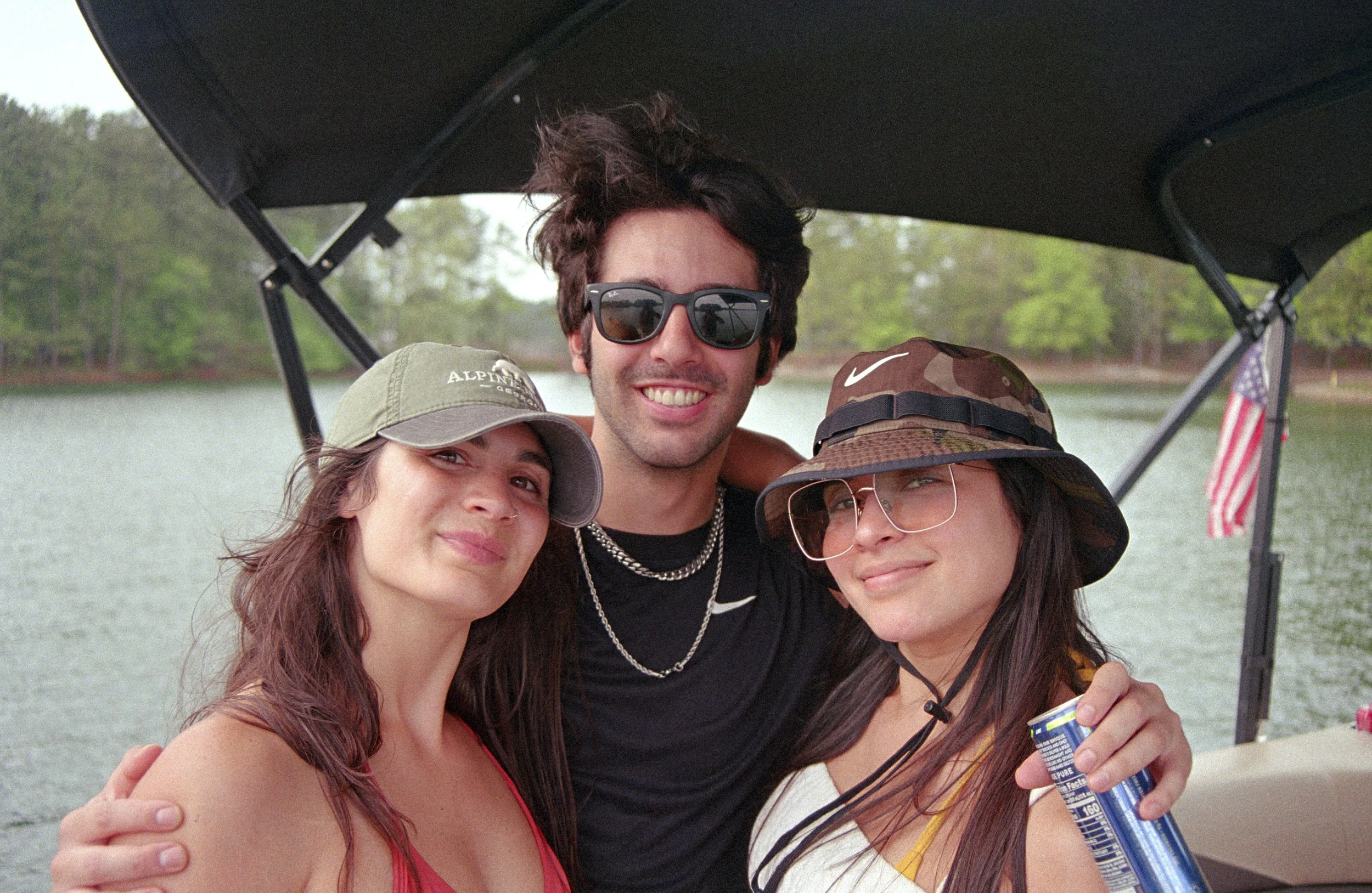Three friends smiling and posing on a boat with water and trees in the background.