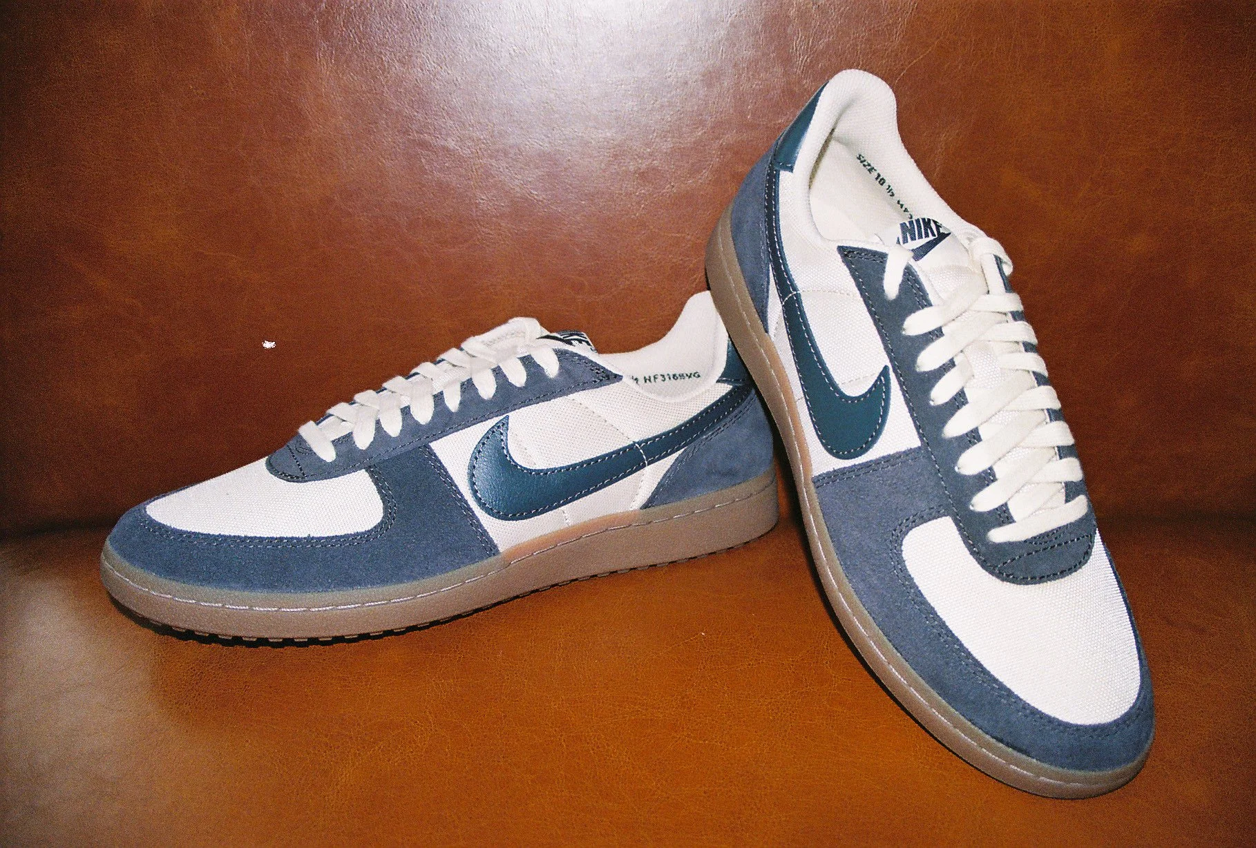Pair of Nike sneakers in white, navy blue, and tan colors on a brown surface.